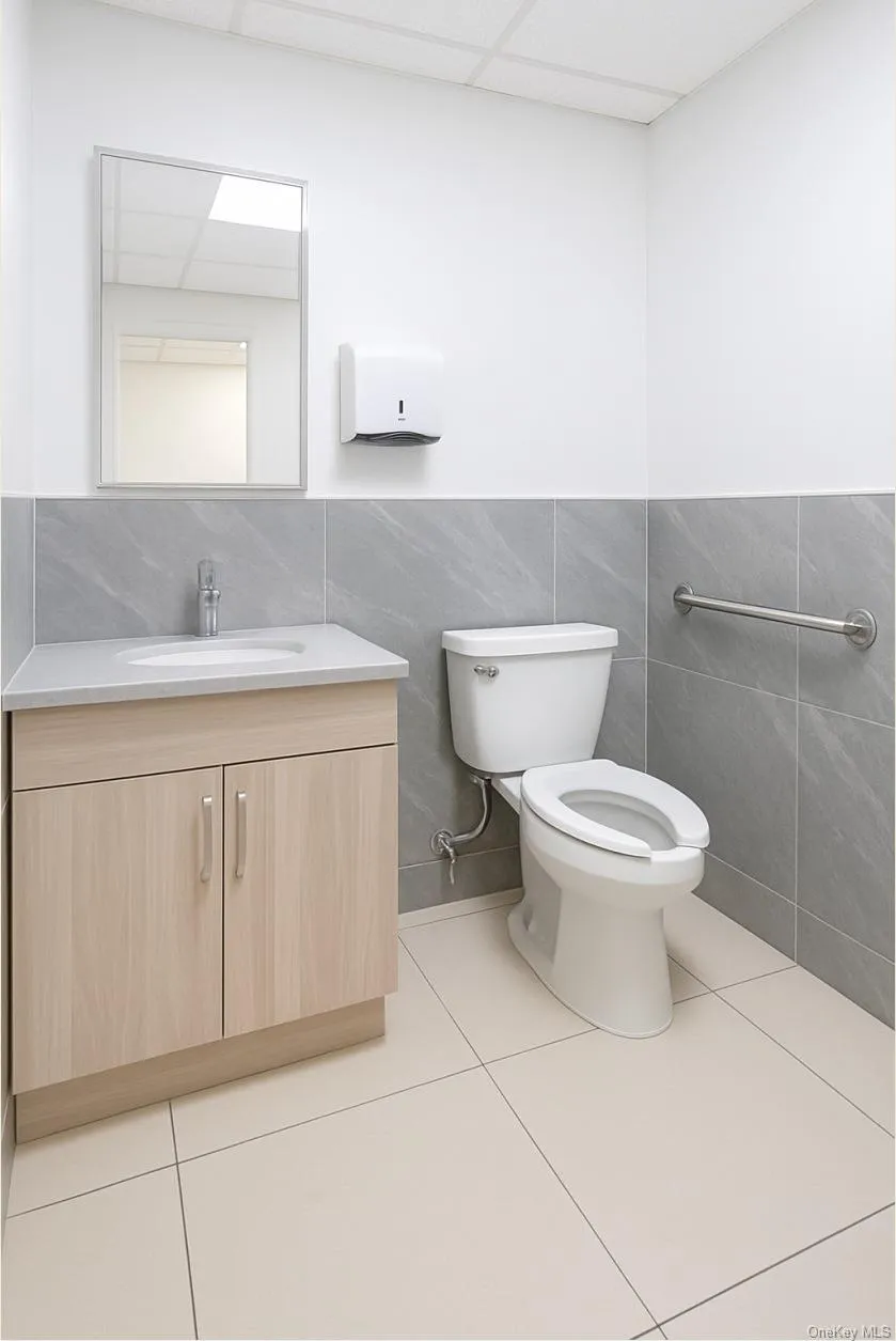 Bathroom featuring a paneled ceiling, tile walls, vanity, and light tile patterned floors Bathroom featuring a paneled ceiling, tile walls, vanity, and light tile patterned floors