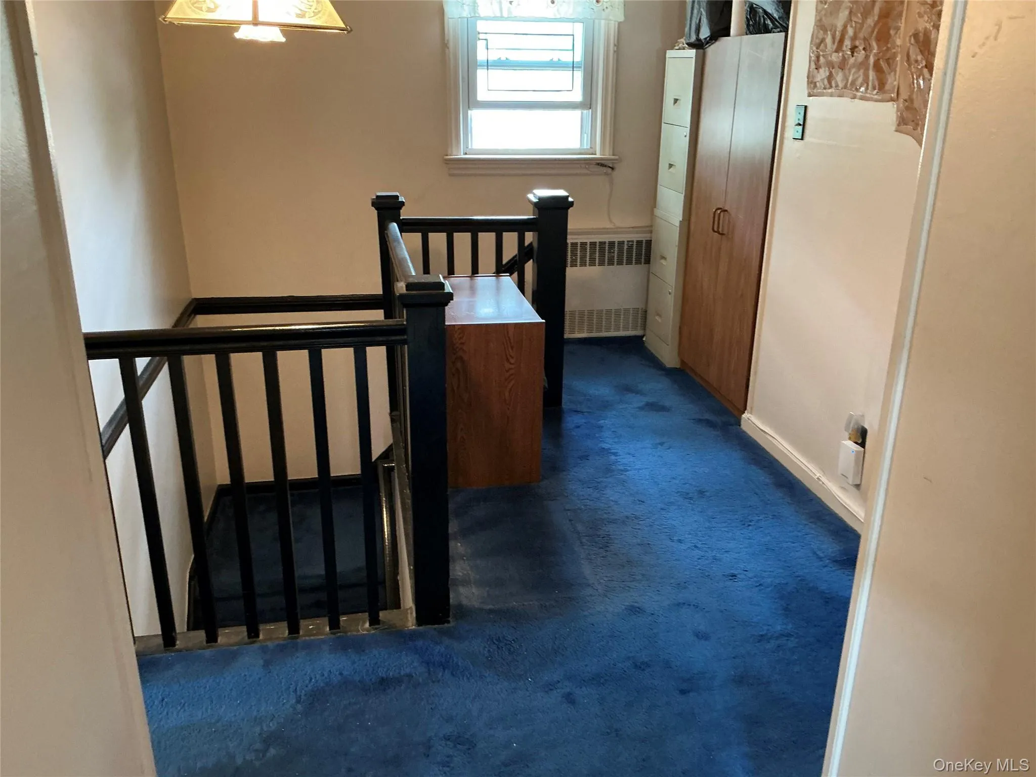 Corridor featuring dark carpet, radiator heating unit, and an upstairs landing Corridor featuring dark carpet, radiator heating unit, and an upstairs landing