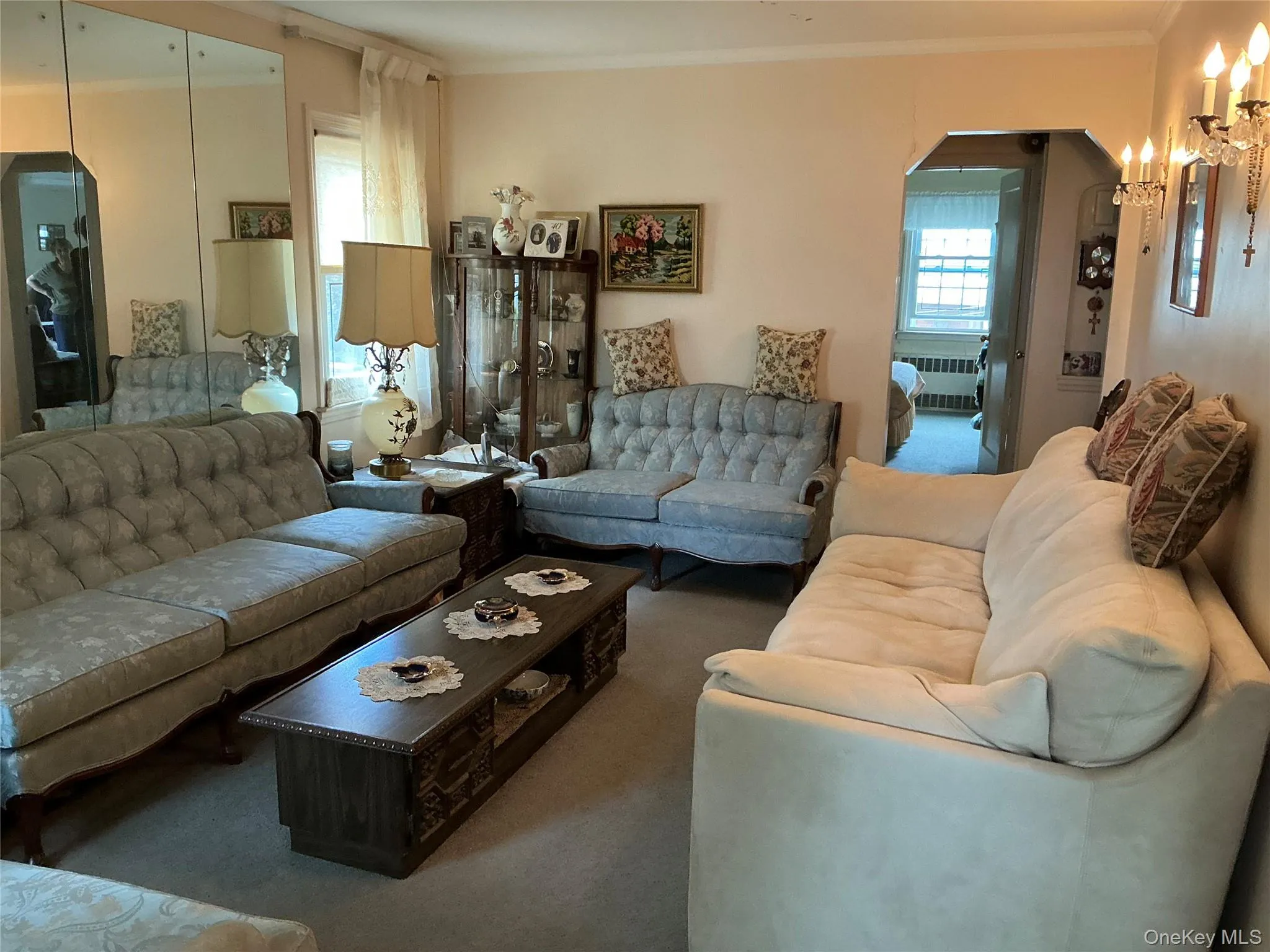 Carpeted living area featuring arched walkways, ornamental molding, and radiator heating unit Carpeted living area featuring arched walkways, ornamental molding, and radiator heating unit