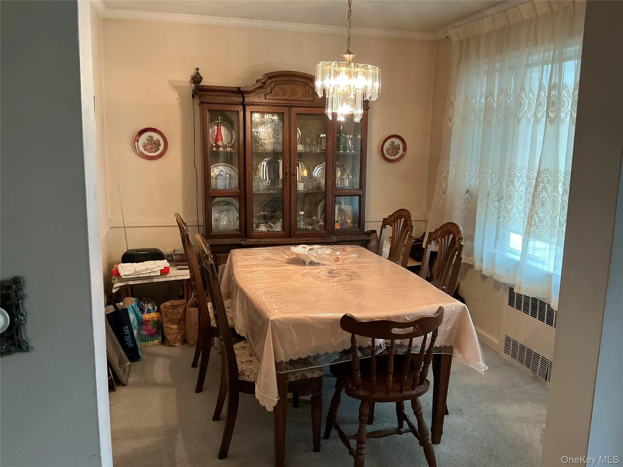 Dining space featuring a chandelier, radiator, ornamental molding, and light carpet Dining space featuring a chandelier, radiator, ornamental molding, and light carpet