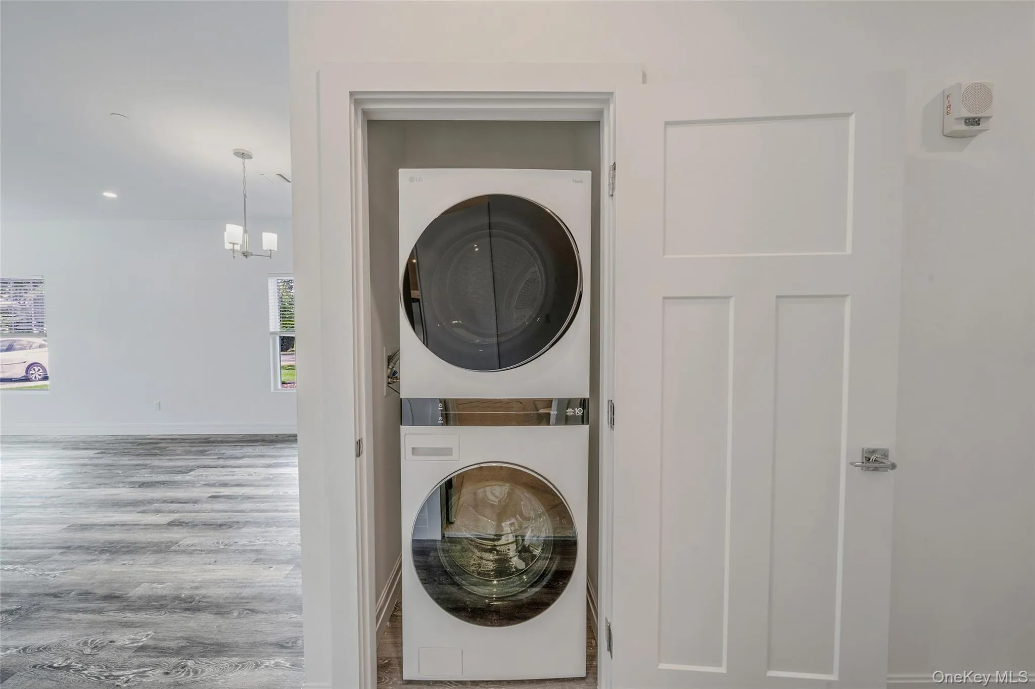 Laundry room with stacked washer / dryer, wood finished floors, and a chandelier Laundry room with stacked washer / dryer, wood finished floors, and a chandelier