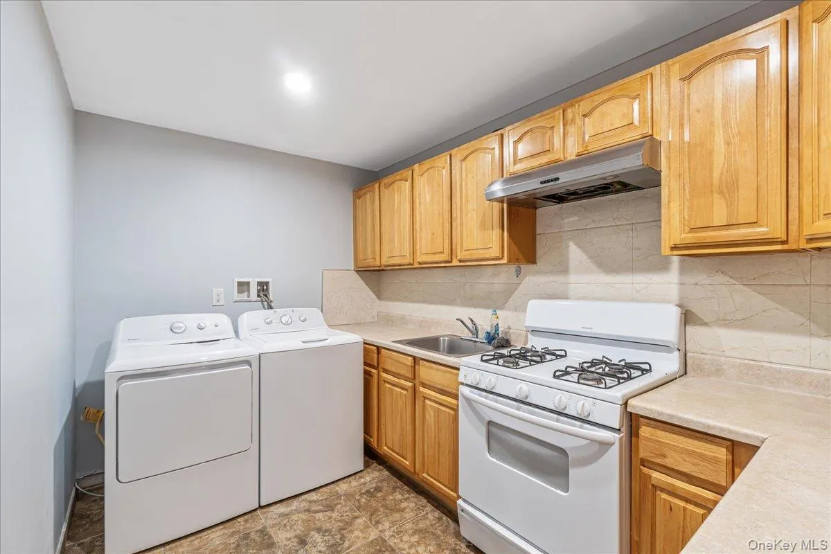 Kitchen featuring white range with gas stovetop, backsplash, under cabinet range hood, light countertops, and washer and dryer Kitchen featuring white range with gas stovetop, backsplash, under cabinet range hood, light countertops, and washer and dryer