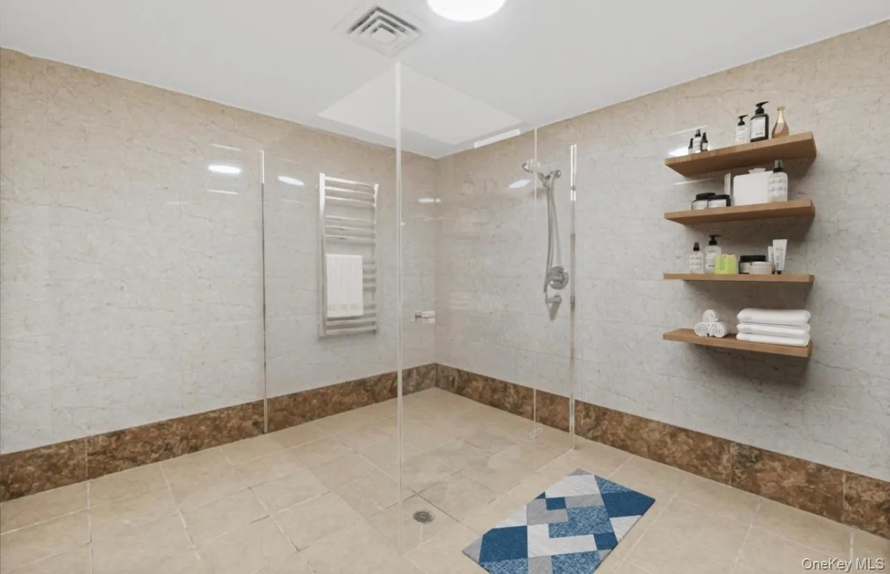 Bathroom featuring walk in shower, radiator, tile walls, a towel warmer, and light tile patterned floors Bathroom featuring walk in shower, radiator, tile walls, a towel warmer, and light tile patterned floors