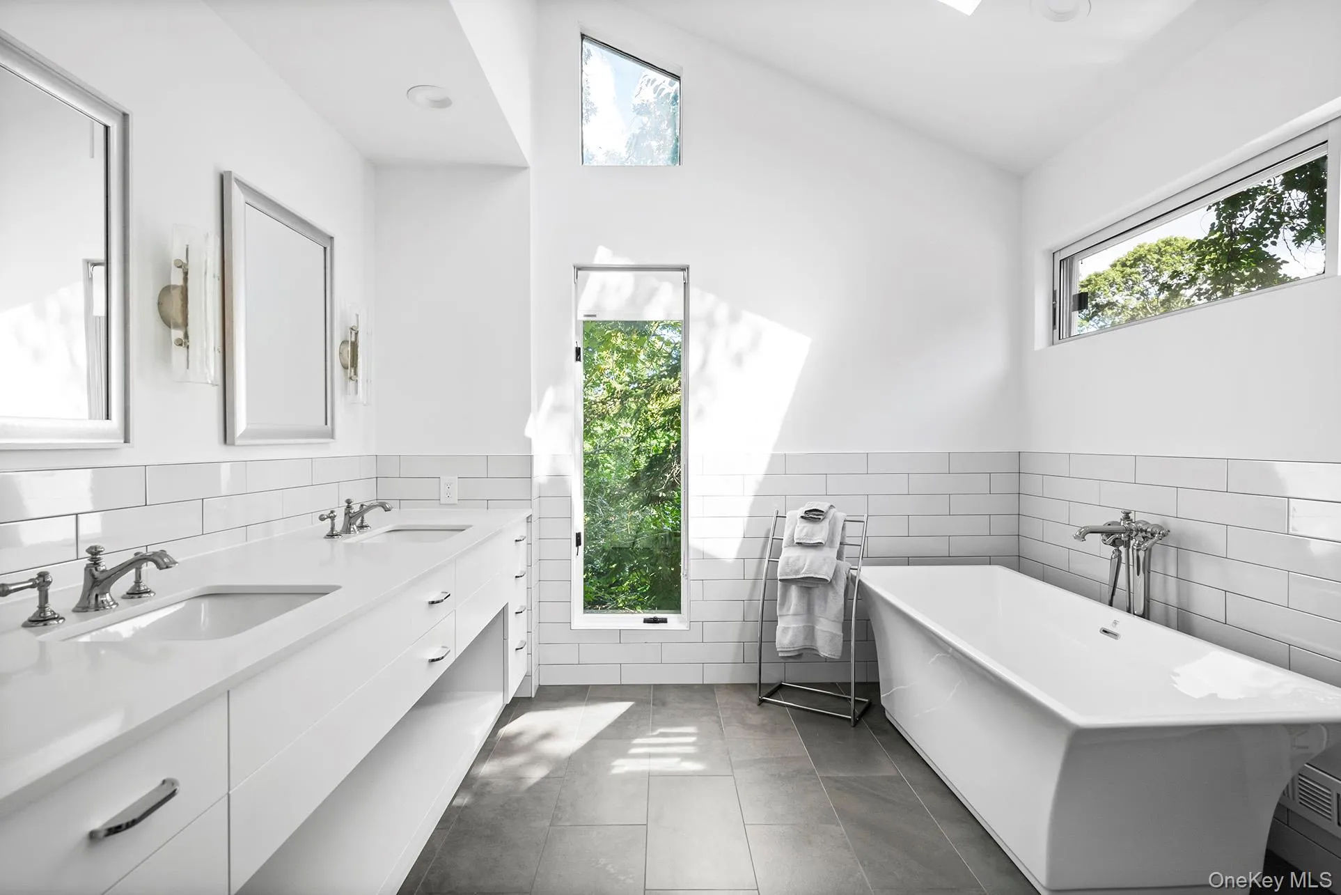Full bathroom featuring double vanity, a freestanding tub, dark tile patterned flooring, tile walls, and a wainscoted wall Full bathroom featuring double vanity, a freestanding tub, dark tile patterned flooring, tile walls, and a wainscoted wall