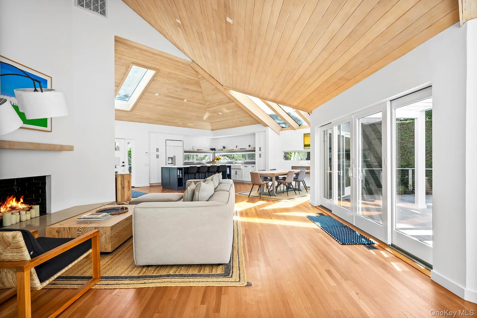 Living room with vaulted ceiling, a warm lit fireplace, plenty of natural light, and wood flooring Living room with vaulted ceiling, a warm lit fireplace, plenty of natural light, and wood flooring