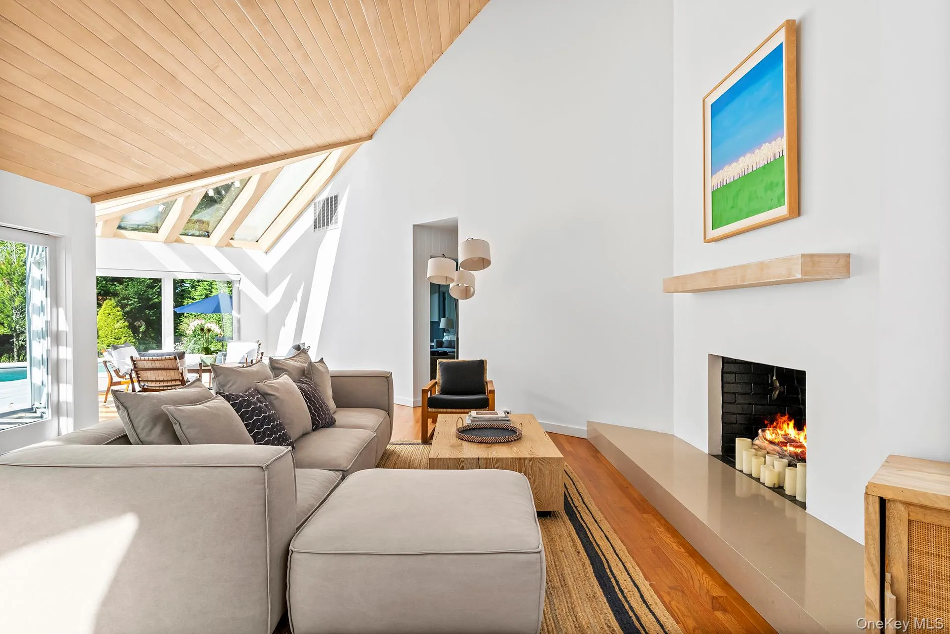 Living room with a lit fireplace, wood finished floors, wood ceiling, a skylight, and high vaulted ceiling Living room with a lit fireplace, wood finished floors, wood ceiling, a skylight, and high vaulted ceiling