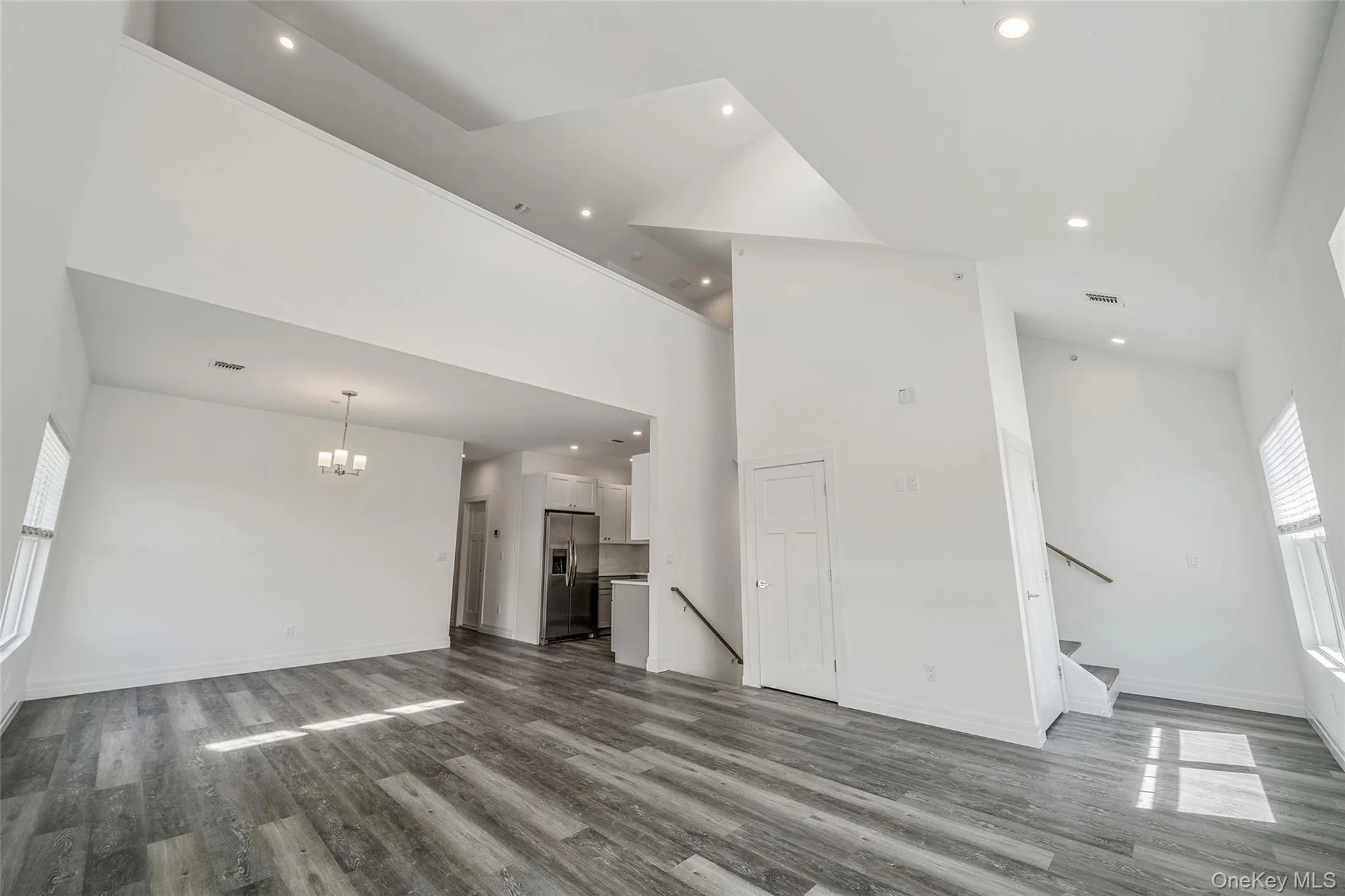 Unfurnished living room featuring high vaulted ceiling, recessed lighting, dark wood-type flooring, a chandelier, and stairs Unfurnished living room featuring high vaulted ceiling, recessed lighting, dark wood-type flooring, a chandelier, and stairs