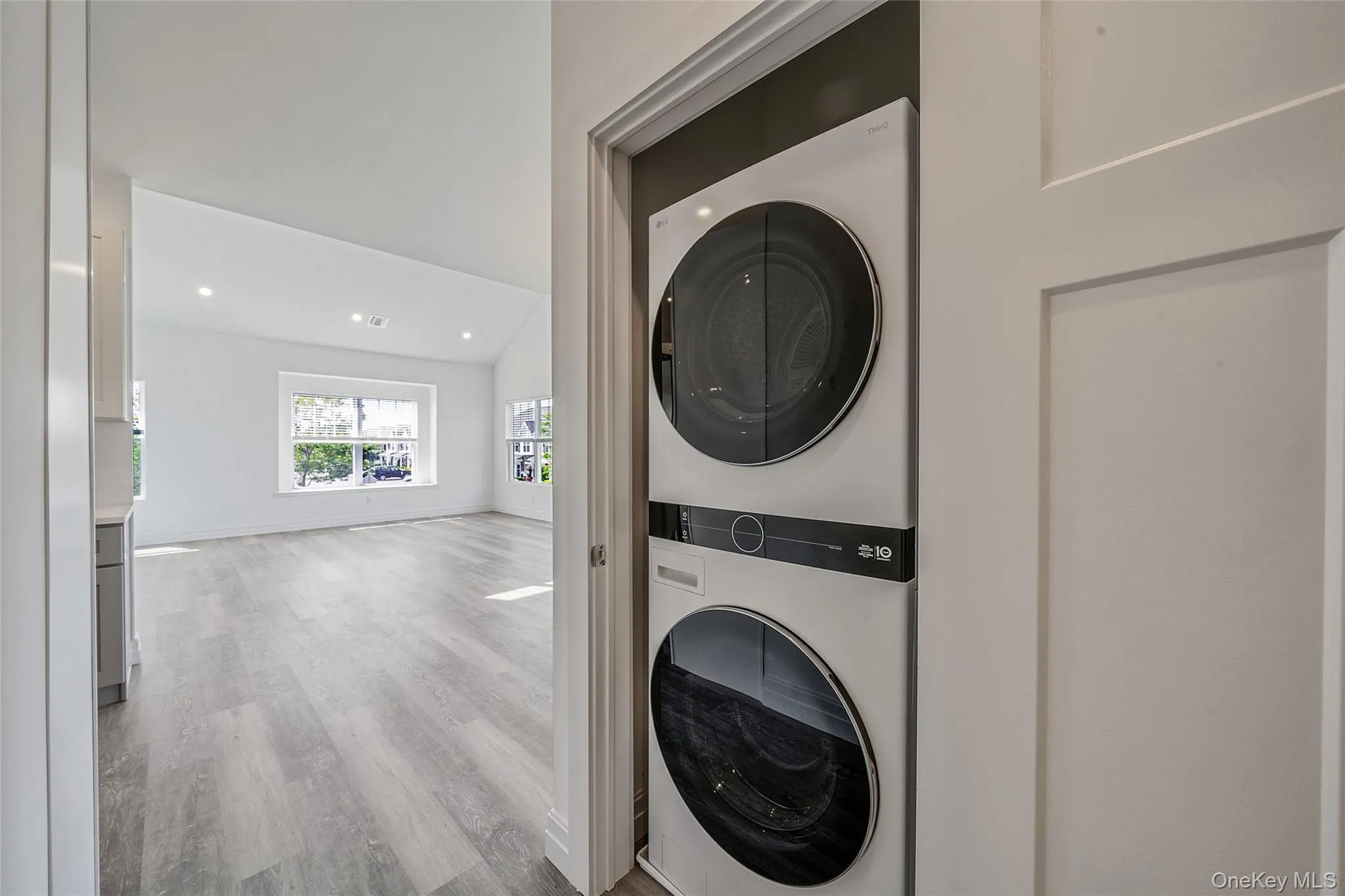 Laundry room featuring estacked washer and dryer, wood finished floors, and recessed lighting Laundry room featuring estacked washer and dryer, wood finished floors, and recessed lighting
