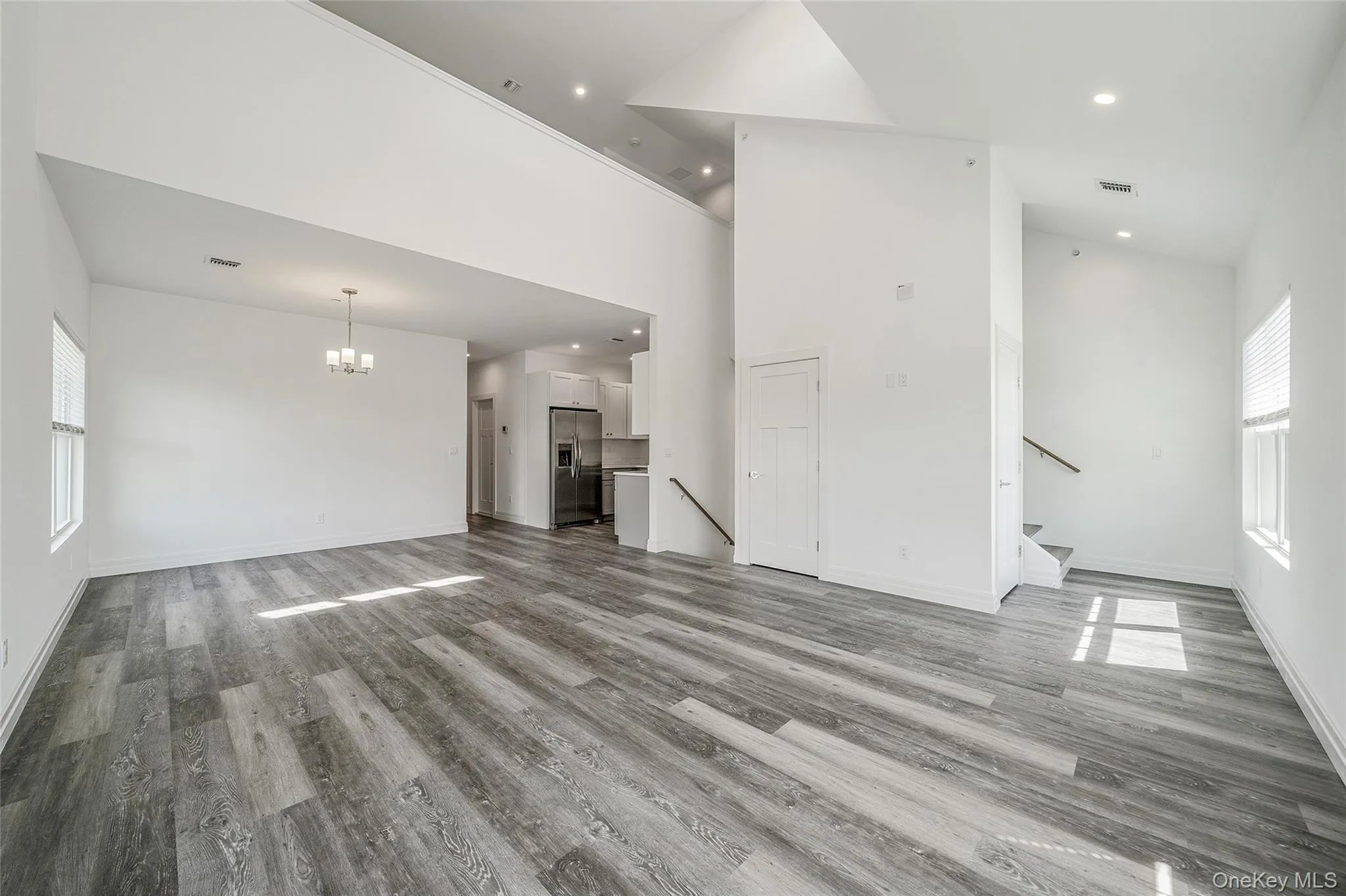 Unfurnished living room with high vaulted ceiling, light wood-style flooring, recessed lighting, a chandelier, and stairs Unfurnished living room with high vaulted ceiling, light wood-style flooring, recessed lighting, a chandelier, and stairs