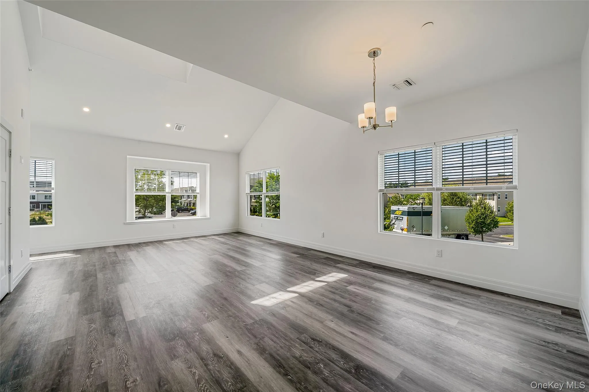 Unfurnished living room featuring wood finished floors, high vaulted ceiling, a chandelier, and recessed lighting Unfurnished living room featuring wood finished floors, high vaulted ceiling, a chandelier, and recessed lighting