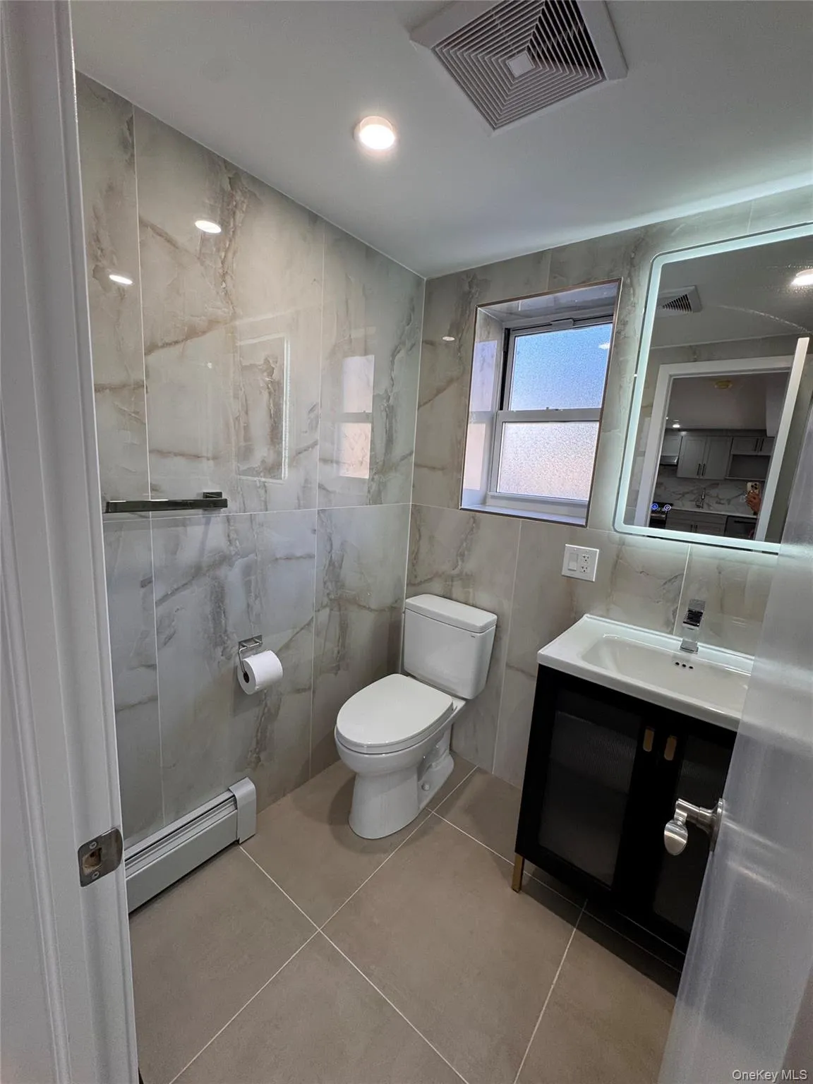 Bathroom with tile walls, a baseboard heating unit, vanity, and light tile patterned floors Bathroom with tile walls, a baseboard heating unit, vanity, and light tile patterned floors