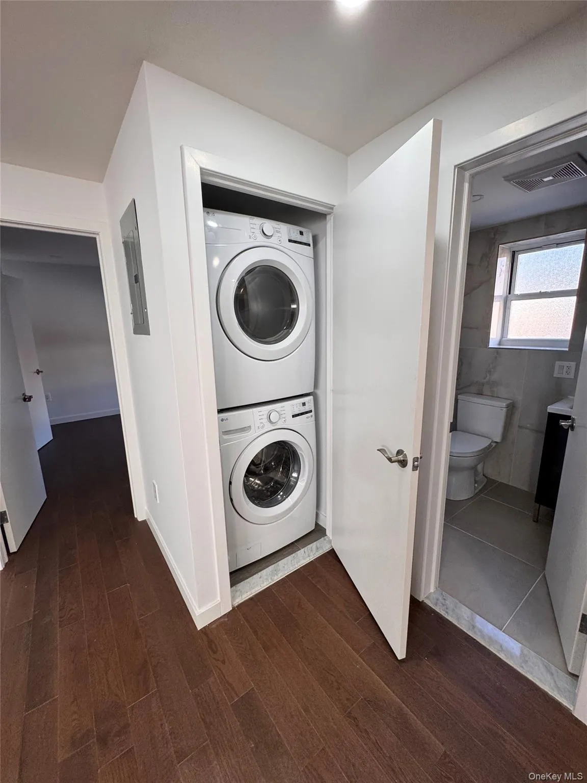 Washroom featuring stacked washing machine and dryer, dark wood-type flooring, and electric panel Washroom featuring stacked washing machine and dryer, dark wood-type flooring, and electric panel