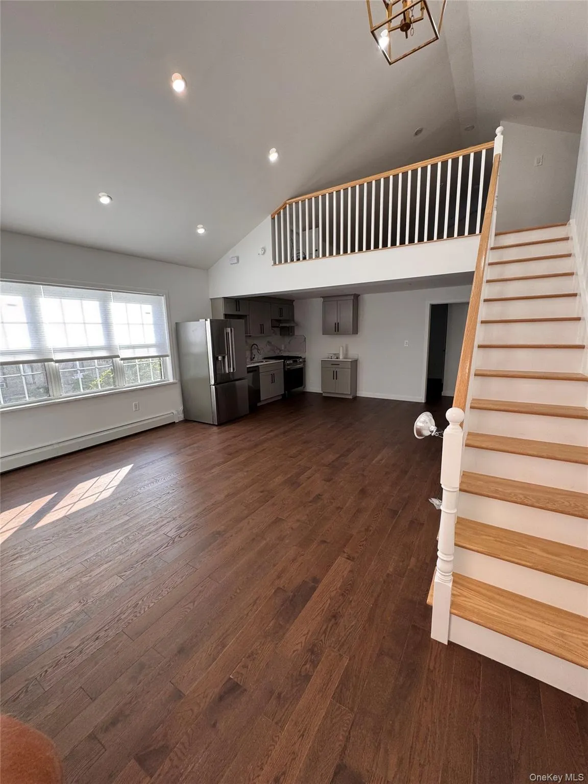 Unfurnished living room featuring a baseboard heating unit, stairs, dark wood-style flooring, recessed lighting, and high vaulted ceiling Unfurnished living room featuring a baseboard heating unit, stairs, dark wood-style flooring, recessed lighting, and high vaulted ceiling