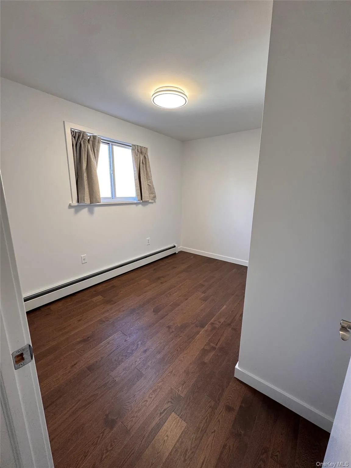 Empty room featuring baseboard heating and dark wood-style flooring Empty room featuring baseboard heating and dark wood-style flooring