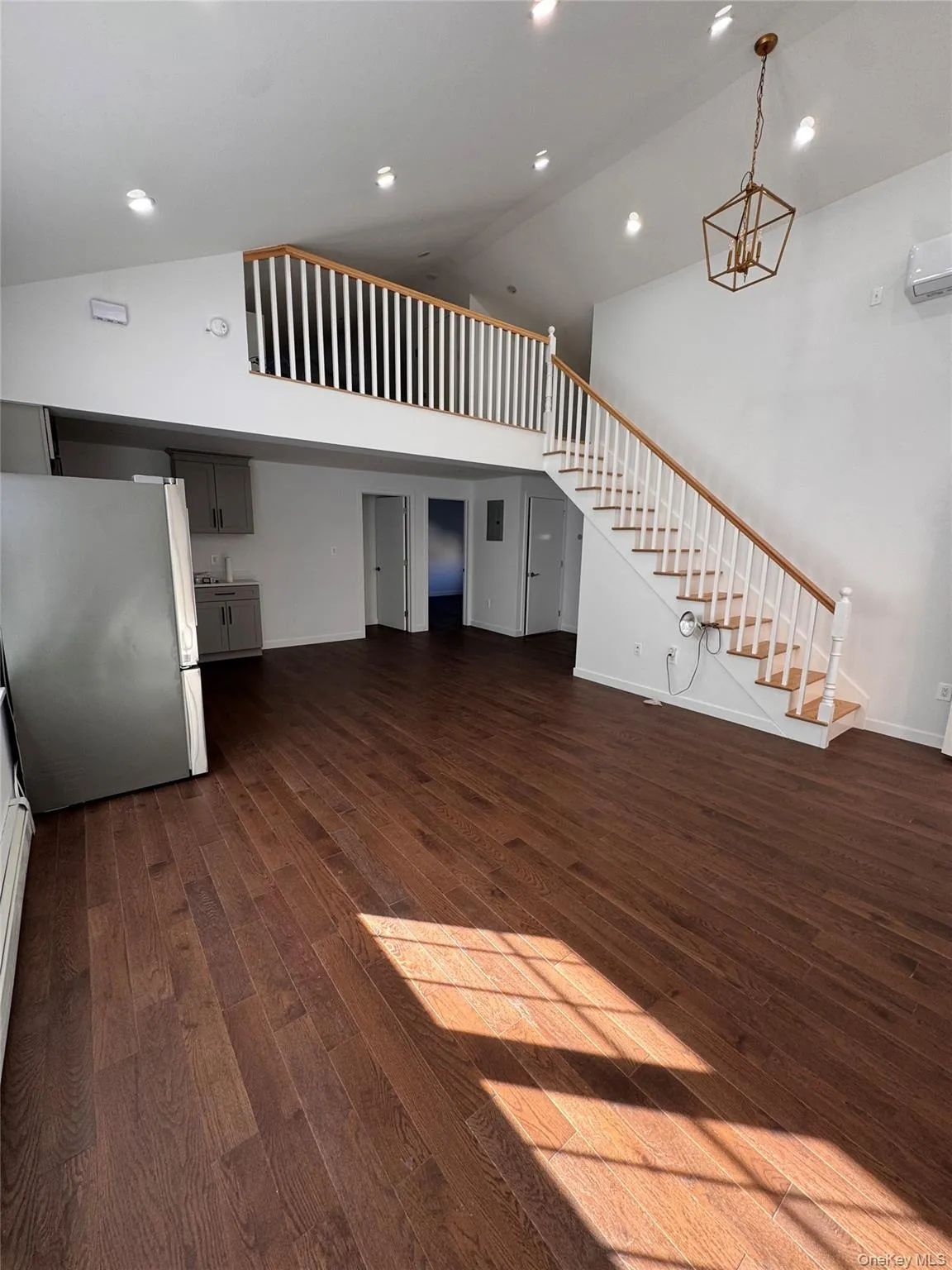 Unfurnished living room with dark wood finished floors, high vaulted ceiling, stairway, recessed lighting, and an AC wall unit Unfurnished living room with dark wood finished floors, high vaulted ceiling, stairway, recessed lighting, and an AC wall unit