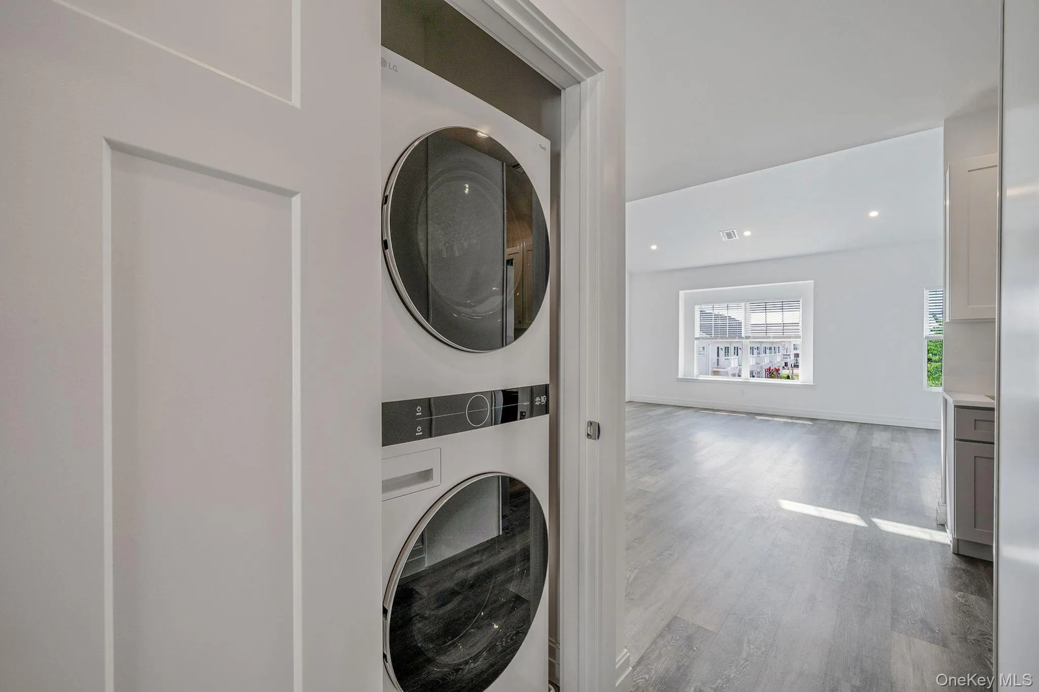 Washroom with estacked washer and dryer, wood finished floors, and recessed lighting Washroom with estacked washer and dryer, wood finished floors, and recessed lighting