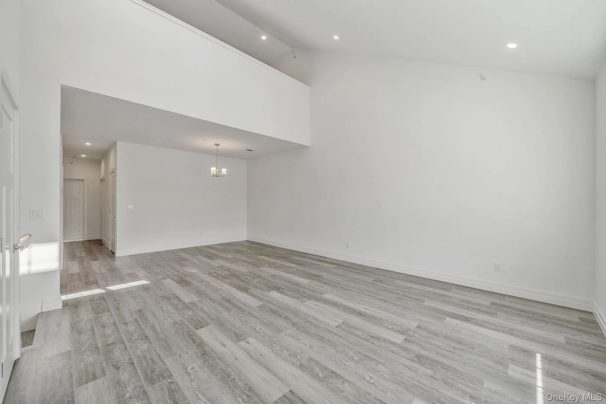 Unfurnished living room with recessed lighting, high vaulted ceiling, light wood-style flooring, and a chandelier Unfurnished living room with recessed lighting, high vaulted ceiling, light wood-style flooring, and a chandelier