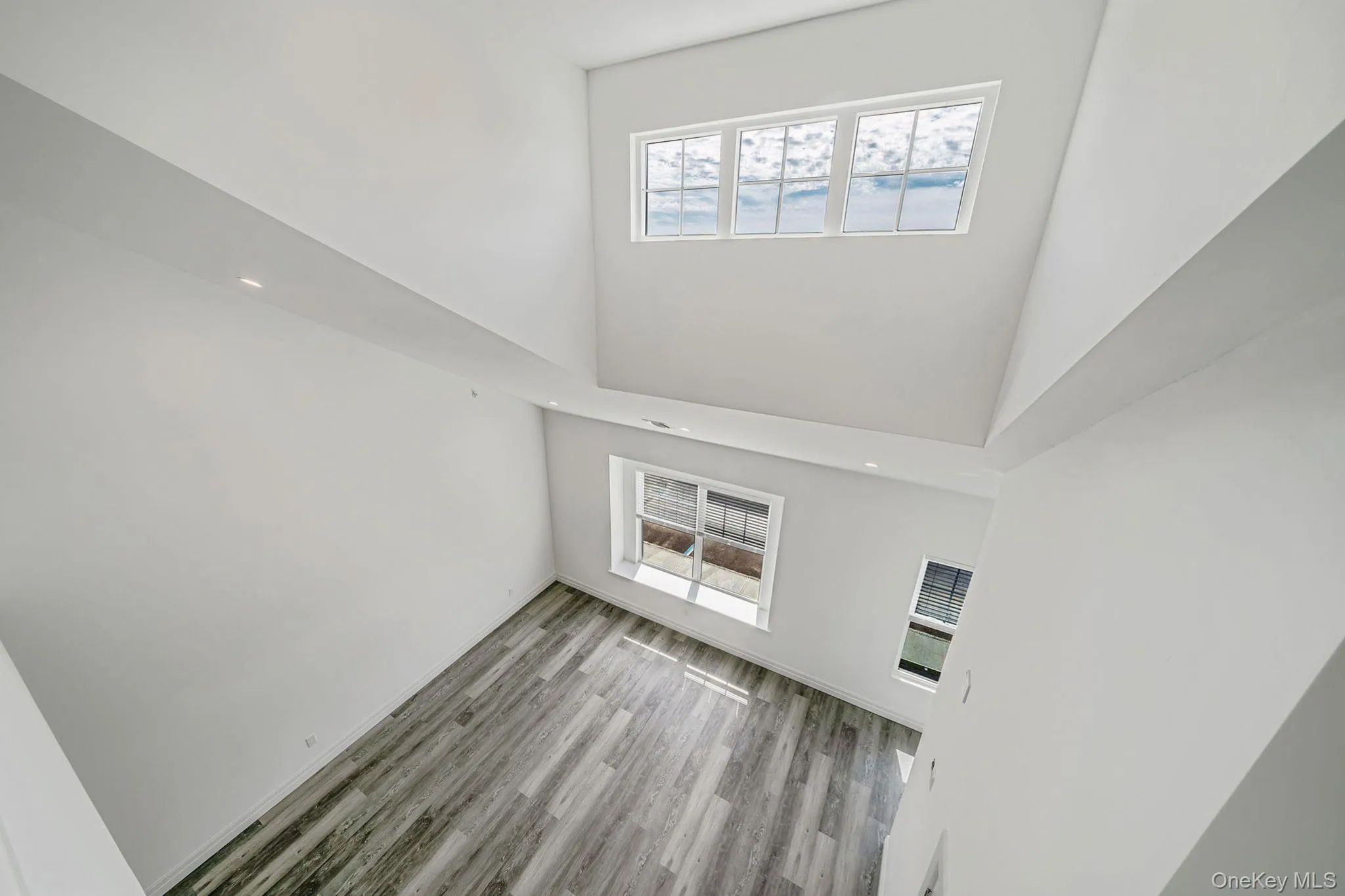 Unfurnished living room featuring a high ceiling, light wood-style flooring, and recessed lighting Unfurnished living room featuring a high ceiling, light wood-style flooring, and recessed lighting