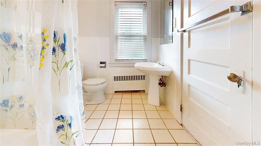 Bathroom featuring light tile patterned floors, radiator, a shower with shower curtain, and tile walls Bathroom featuring light tile patterned floors, radiator, a shower with shower curtain, and tile walls