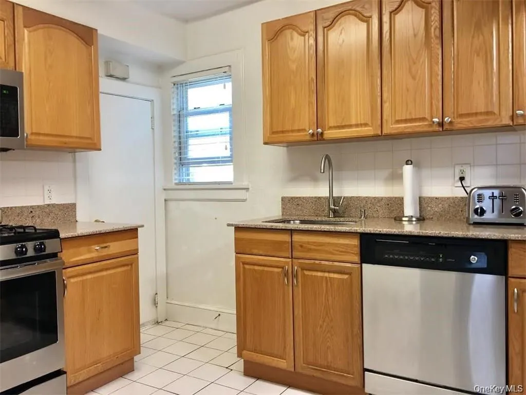 Kitchen with decorative backsplash, appliances with stainless steel finishes, light tile patterned floors, light stone countertops, and brown cabinets Kitchen with decorative backsplash, appliances with stainless steel finishes, light tile patterned floors, light stone countertops, and brown cabinets