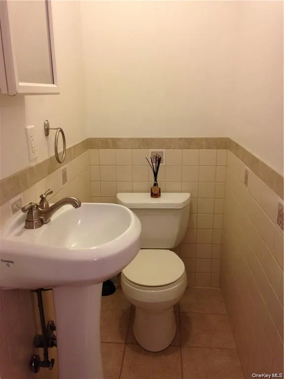 Half bath featuring tile walls, light tile patterned floors, and wainscoting Half bath featuring tile walls, light tile patterned floors, and wainscoting