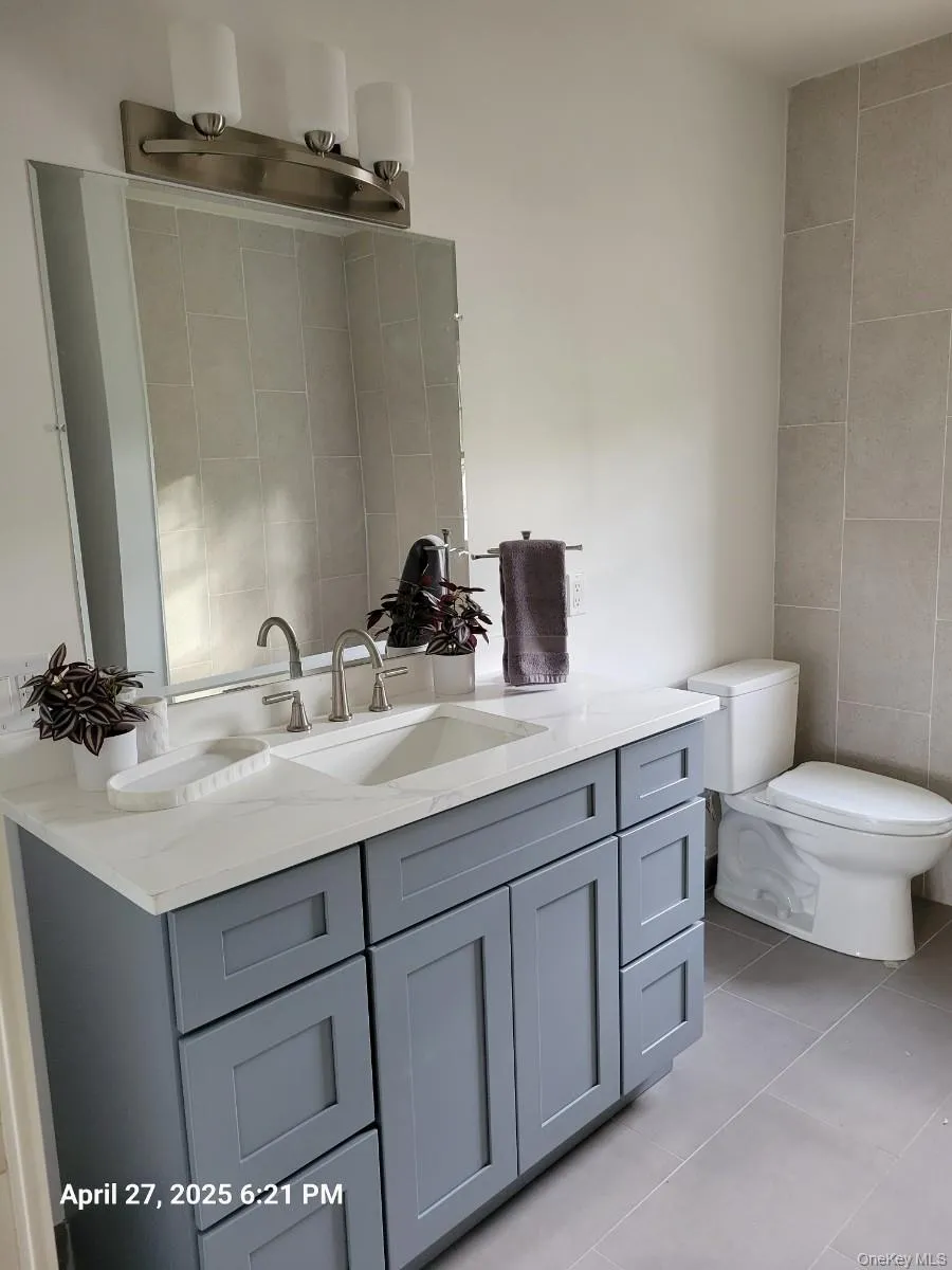 Full bath featuring double vanity, light tile patterned floors, and tile walls Full bath featuring double vanity, light tile patterned floors, and tile walls