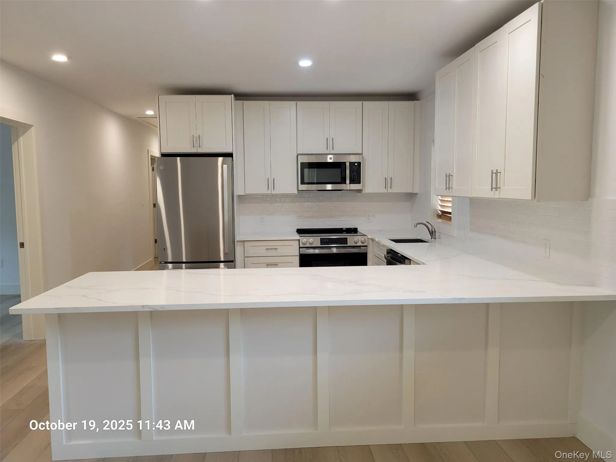 Kitchen with appliances with stainless steel finishes, a peninsula, light wood-style flooring, light stone countertops, and white cabinetry Kitchen with appliances with stainless steel finishes, a peninsula, light wood-style flooring, light stone countertops, and white cabinetry