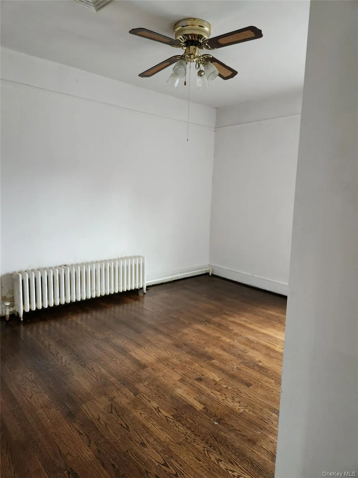 Spare room featuring radiator, dark wood-style flooring, and a ceiling fan Spare room featuring radiator, dark wood-style flooring, and a ceiling fan