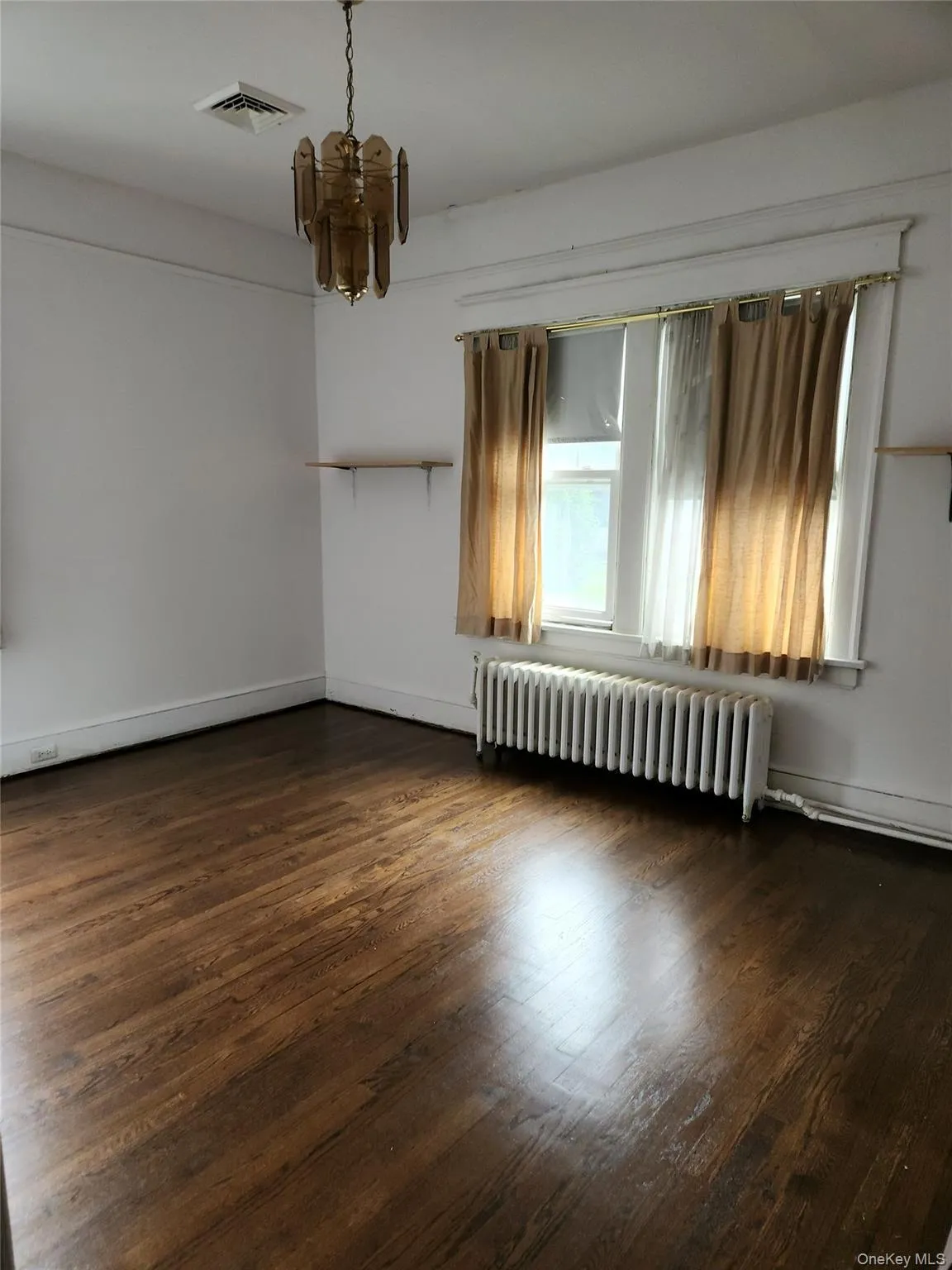 Unfurnished room with dark wood-style flooring, radiator, and a chandelier Unfurnished room with dark wood-style flooring, radiator, and a chandelier