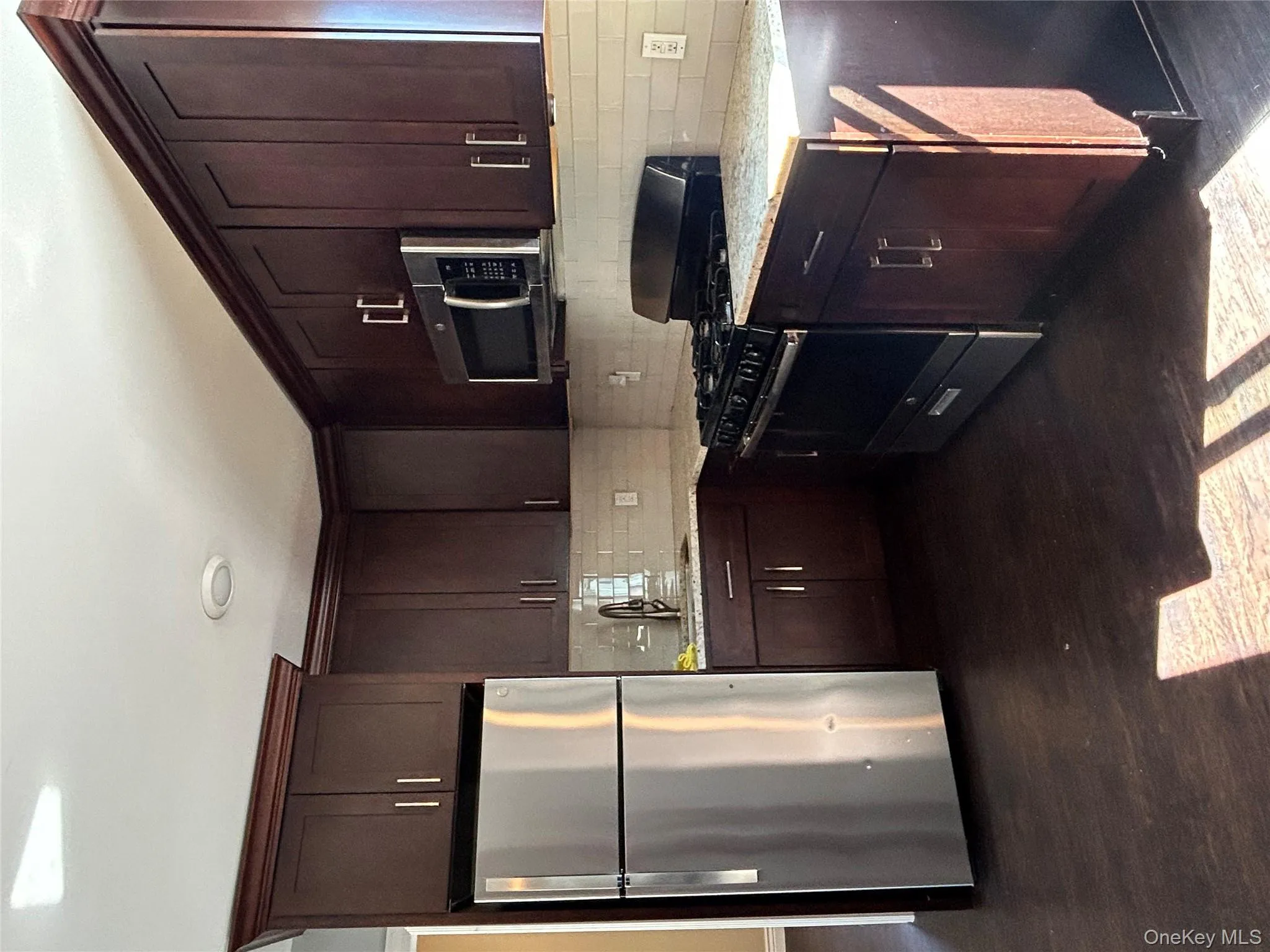 Kitchen with stainless steel range oven, refrigerator, dark brown cabinetry, black microwave, and light stone counters Kitchen with stainless steel range oven, refrigerator, dark brown cabinetry, black microwave, and light stone counters