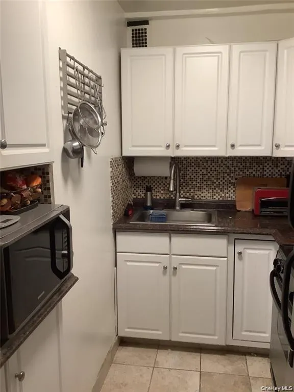 Kitchen with dark countertops, white cabinetry, tasteful backsplash, black stove, and light tile patterned floors Kitchen with dark countertops, white cabinetry, tasteful backsplash, black stove, and light tile patterned floors