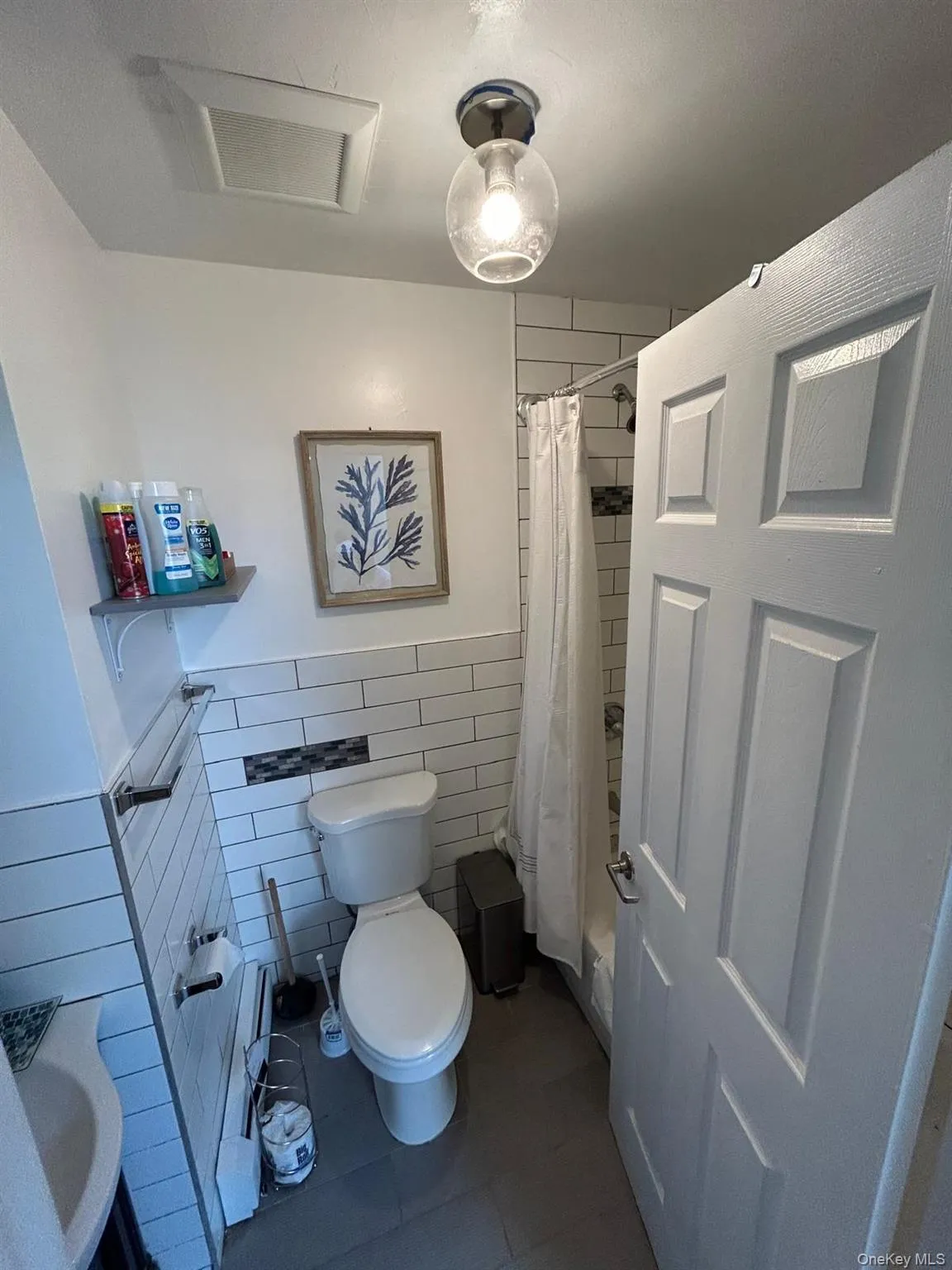 Bathroom featuring tile walls, tile patterned floors, a wainscoted wall, and shower / tub combo with curtain Bathroom featuring tile walls, tile patterned floors, a wainscoted wall, and shower / tub combo with curtain