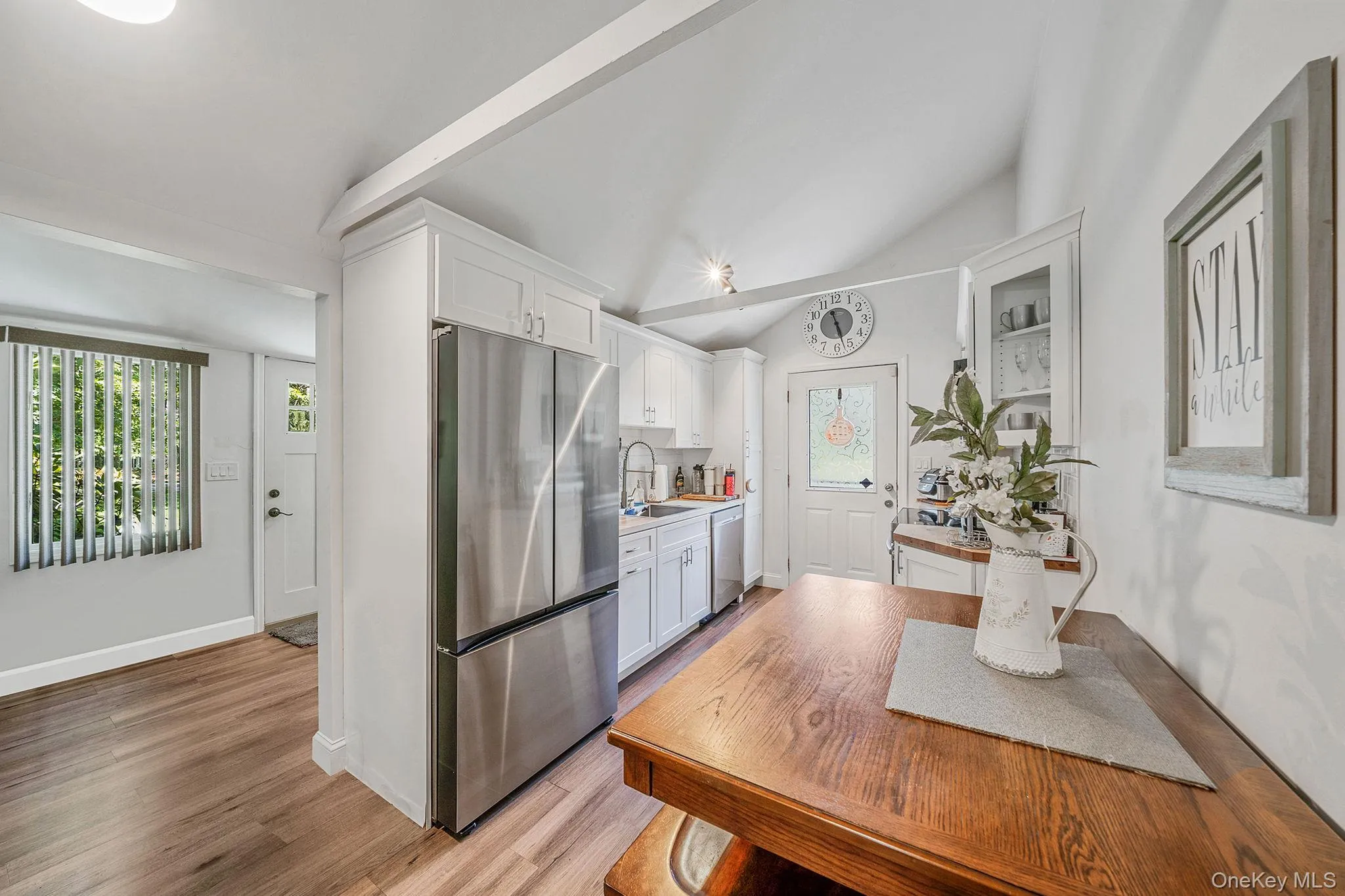 Kitchen featuring white cabinets, stainless steel appliances, light countertops, light wood finished floors, and lofted ceiling Kitchen featuring white cabinets, stainless steel appliances, light countertops, light wood finished floors, and lofted ceiling