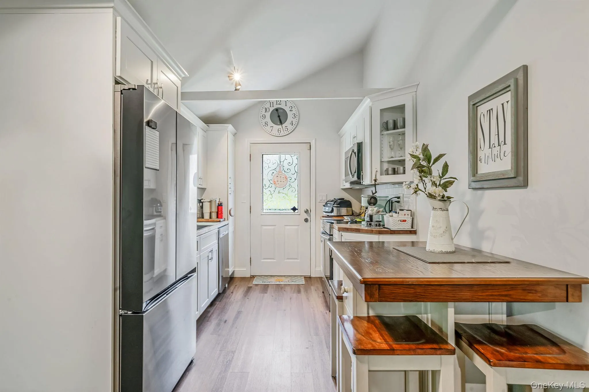 Kitchen featuring white cabinetry, glass insert cabinets, appliances with stainless steel finishes, light wood-type flooring, and lofted ceiling Kitchen featuring white cabinetry, glass insert cabinets, appliances with stainless steel finishes, light wood-type flooring, and lofted ceiling