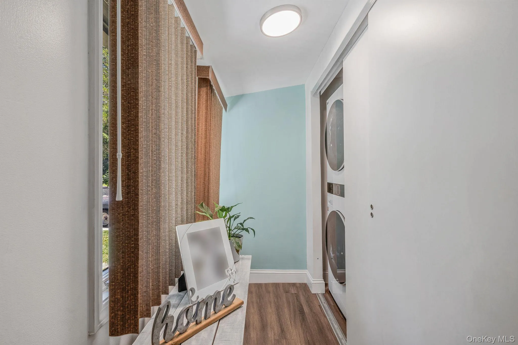 Laundry room featuring healthy amount of natural light, dark wood-type flooring, and stacked washer / drying machine Laundry room featuring healthy amount of natural light, dark wood-type flooring, and stacked washer / drying machine