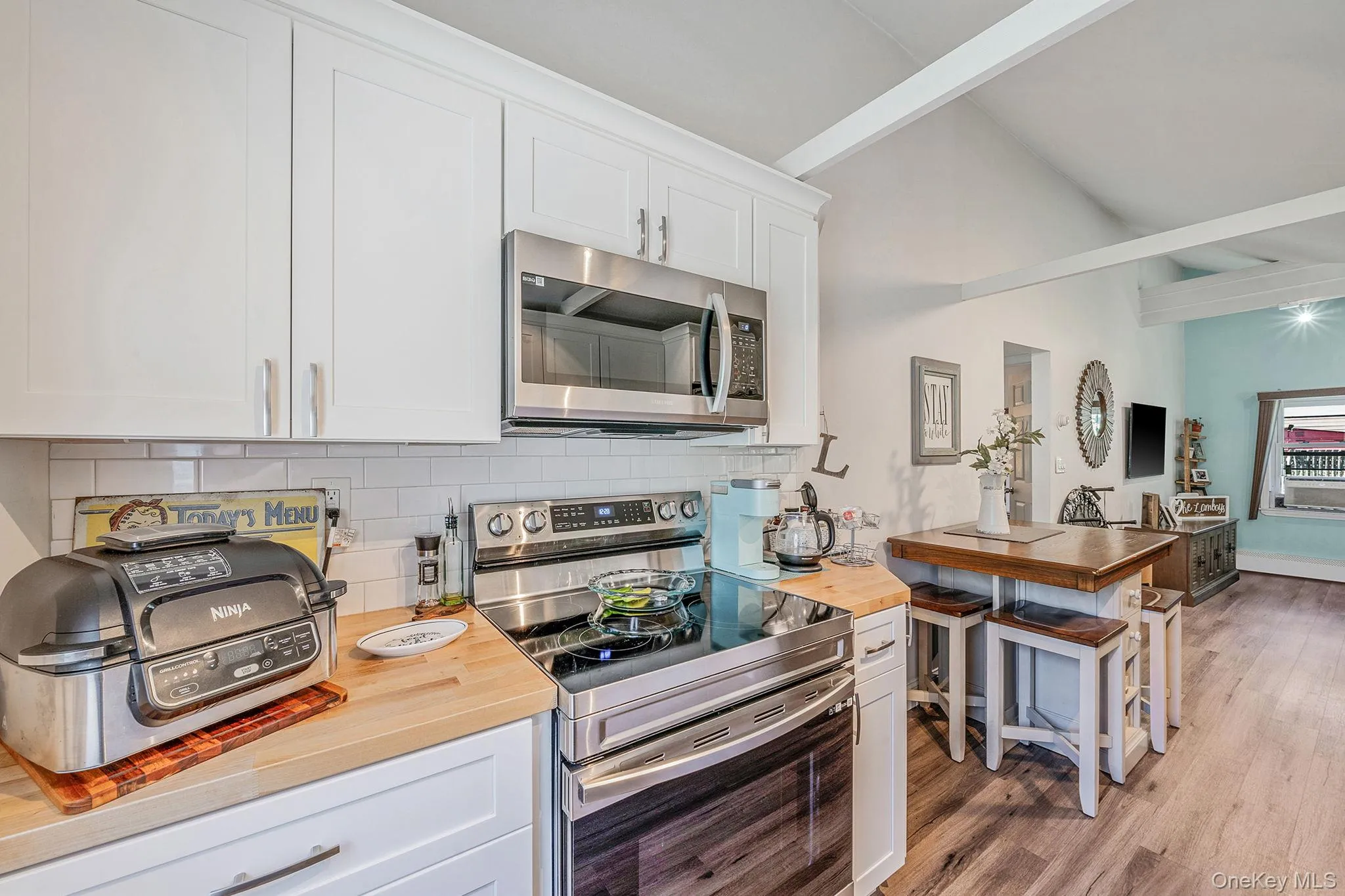 Kitchen featuring appliances with stainless steel finishes, beam ceiling, white cabinets, tasteful backsplash, and wood finished floors Kitchen featuring appliances with stainless steel finishes, beam ceiling, white cabinets, tasteful backsplash, and wood finished floors