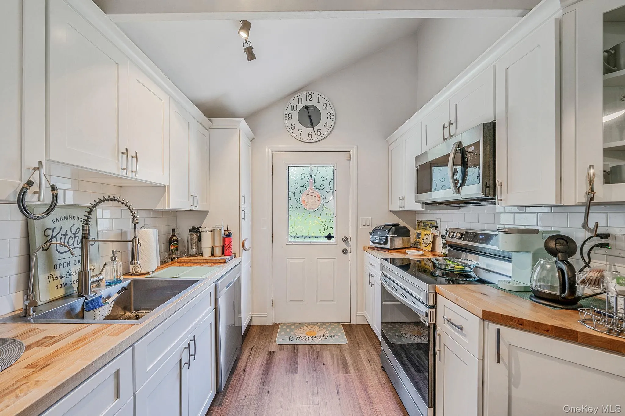 Kitchen with lofted ceiling, stainless steel appliances, white cabinets, tasteful backsplash, and light wood-style flooring Kitchen with lofted ceiling, stainless steel appliances, white cabinets, tasteful backsplash, and light wood-style flooring