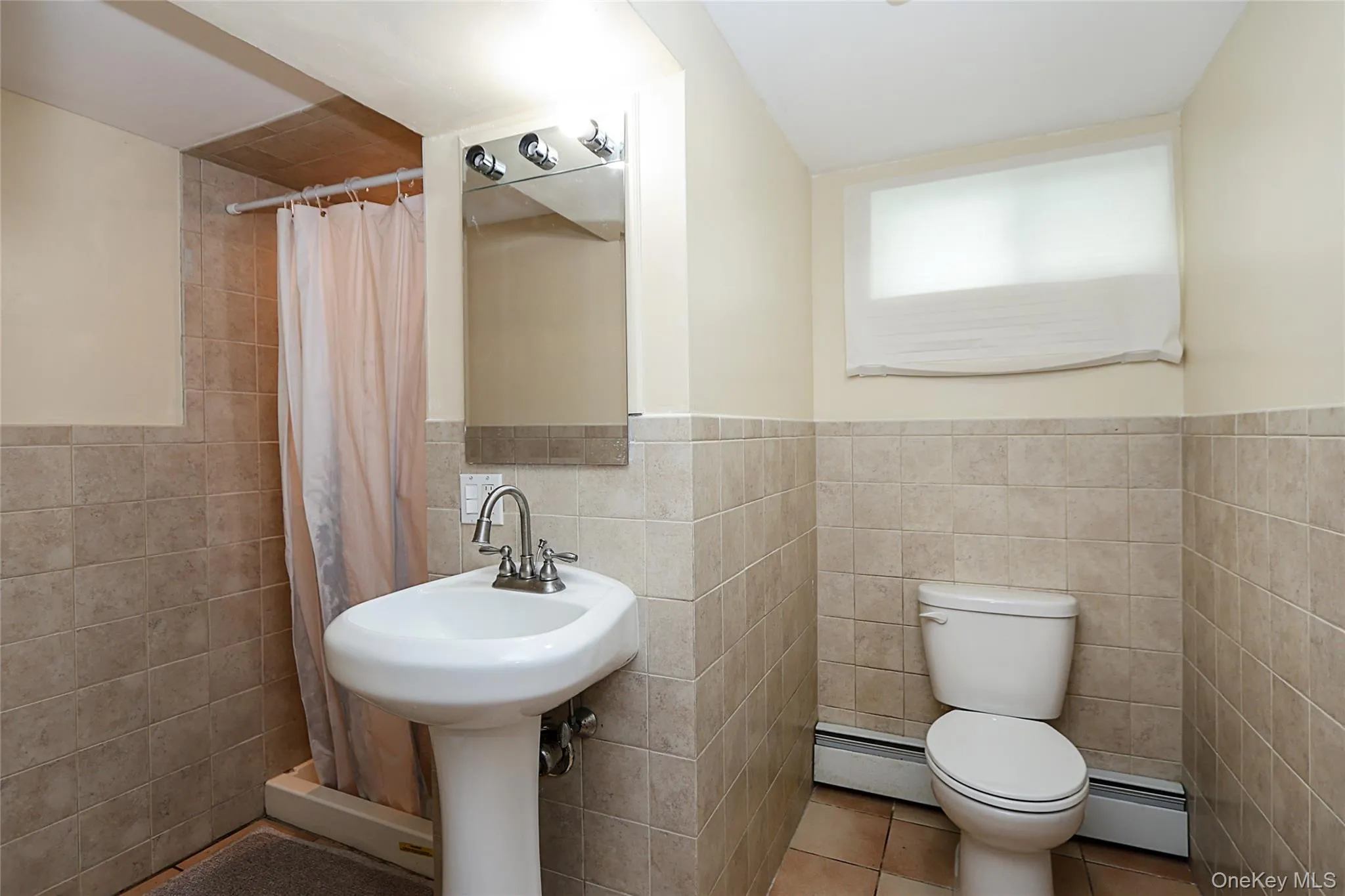 Bathroom with tile patterned floors, baseboard heating, a shower stall, tile walls, and wainscoting Bathroom with tile patterned floors, baseboard heating, a shower stall, tile walls, and wainscoting