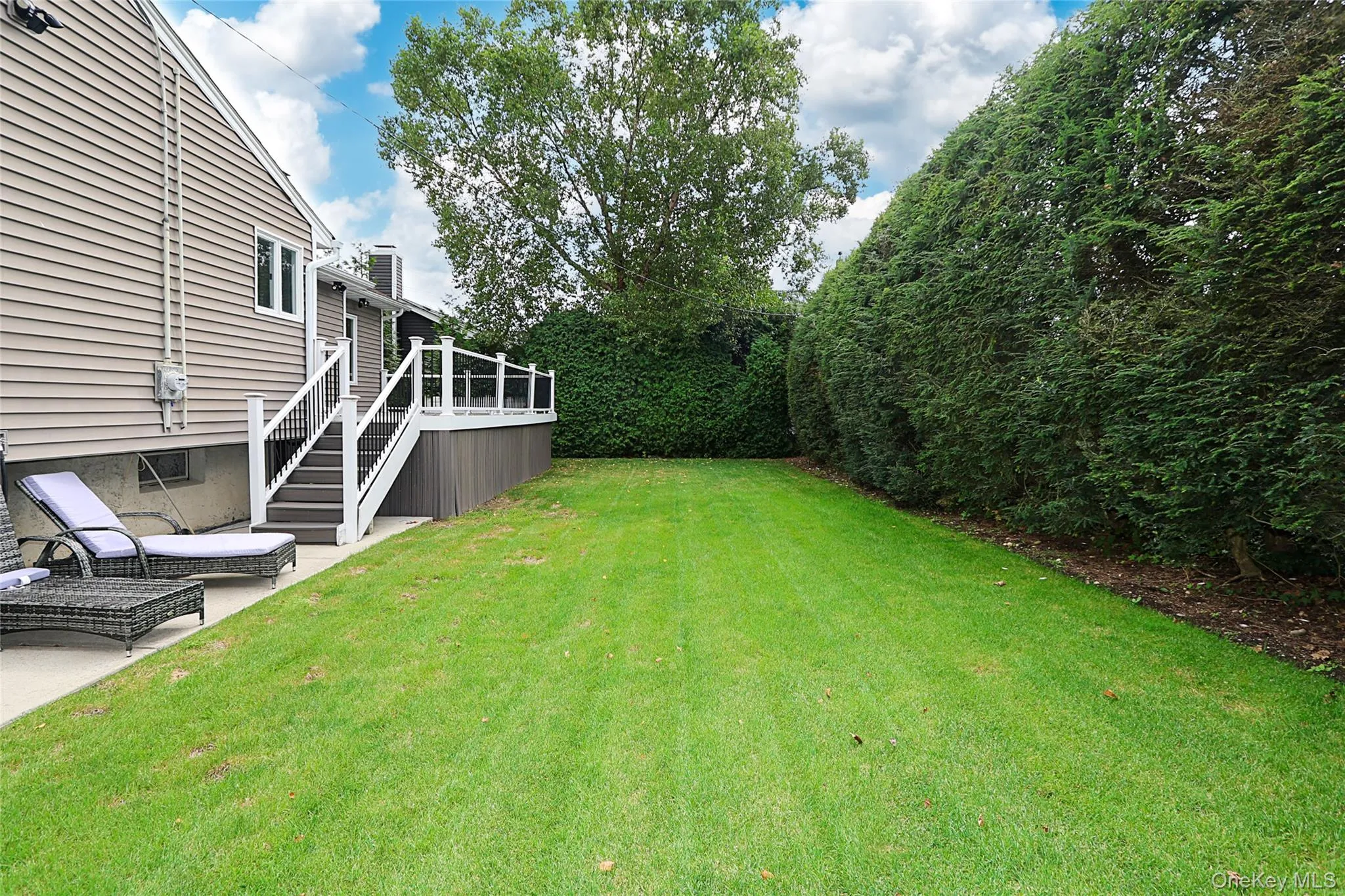 View of green lawn featuring stairs, a deck, and a patio View of green lawn featuring stairs, a deck, and a patio