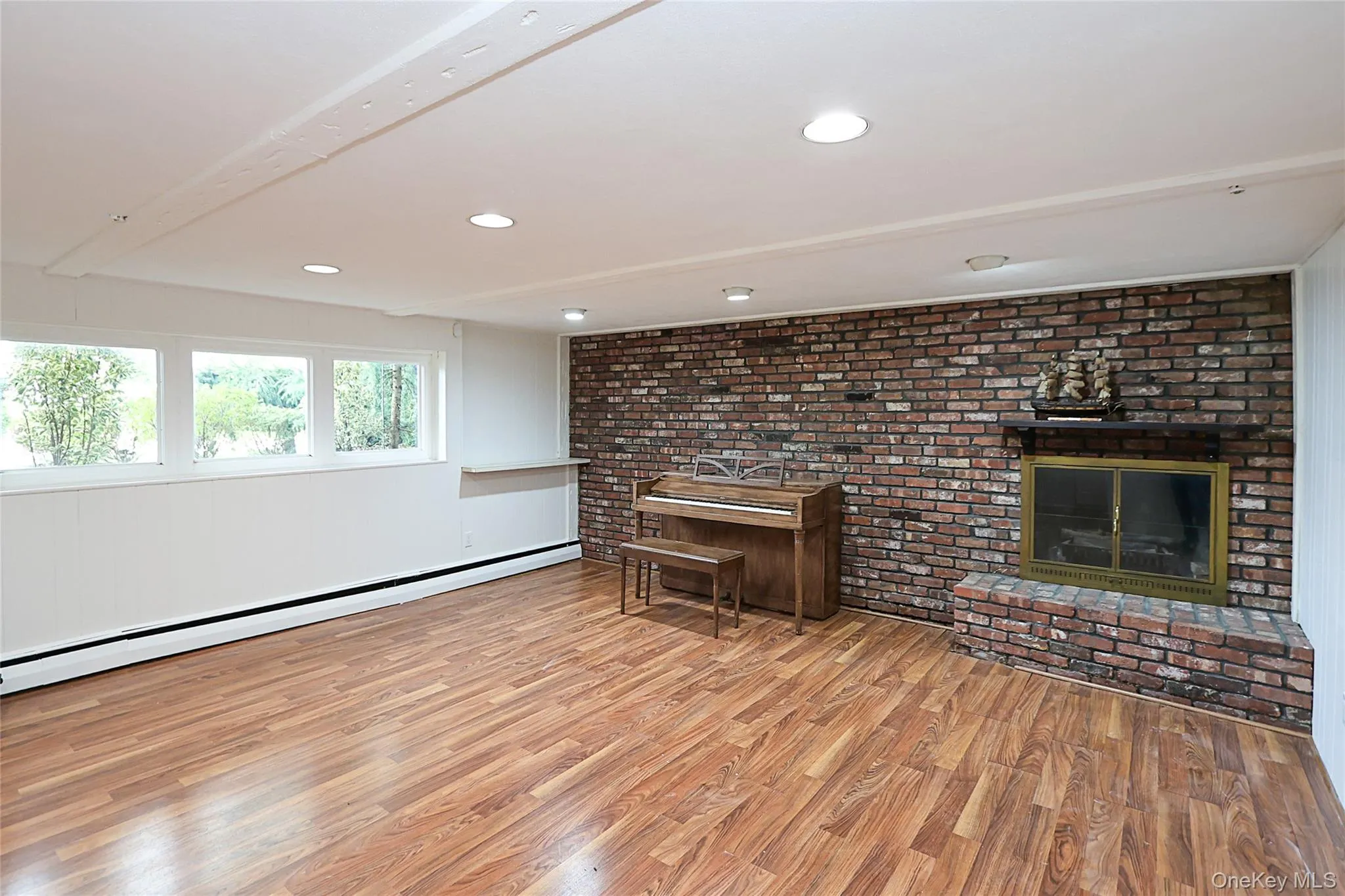 Living room with a fireplace, light wood-style flooring, baseboard heating, recessed lighting, and brick wall Living room with a fireplace, light wood-style flooring, baseboard heating, recessed lighting, and brick wall