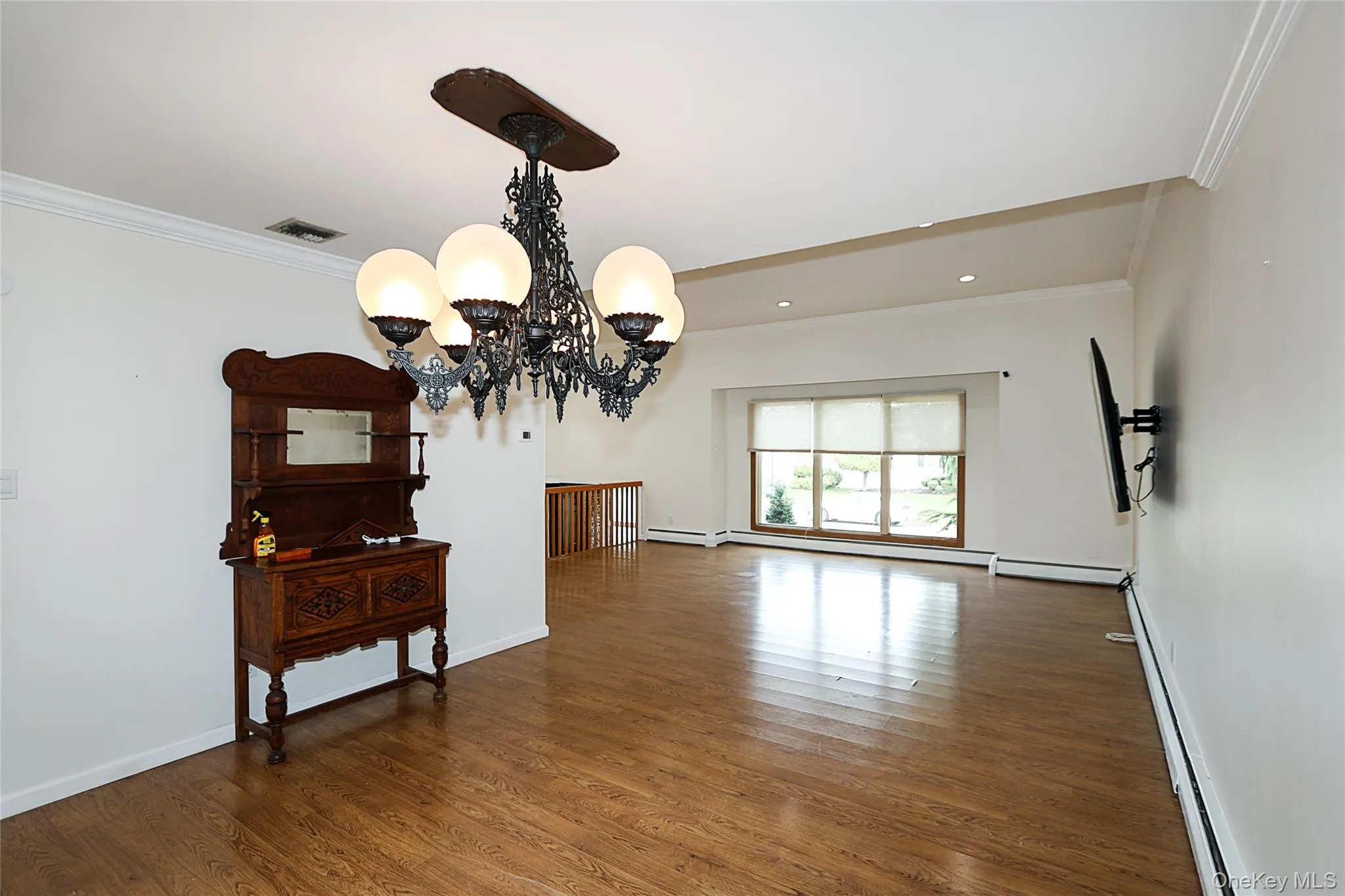 Spare room featuring ornamental molding, wood finished floors, baseboard heating, a chandelier, and a baseboard heating unit Spare room featuring ornamental molding, wood finished floors, baseboard heating, a chandelier, and a baseboard heating unit