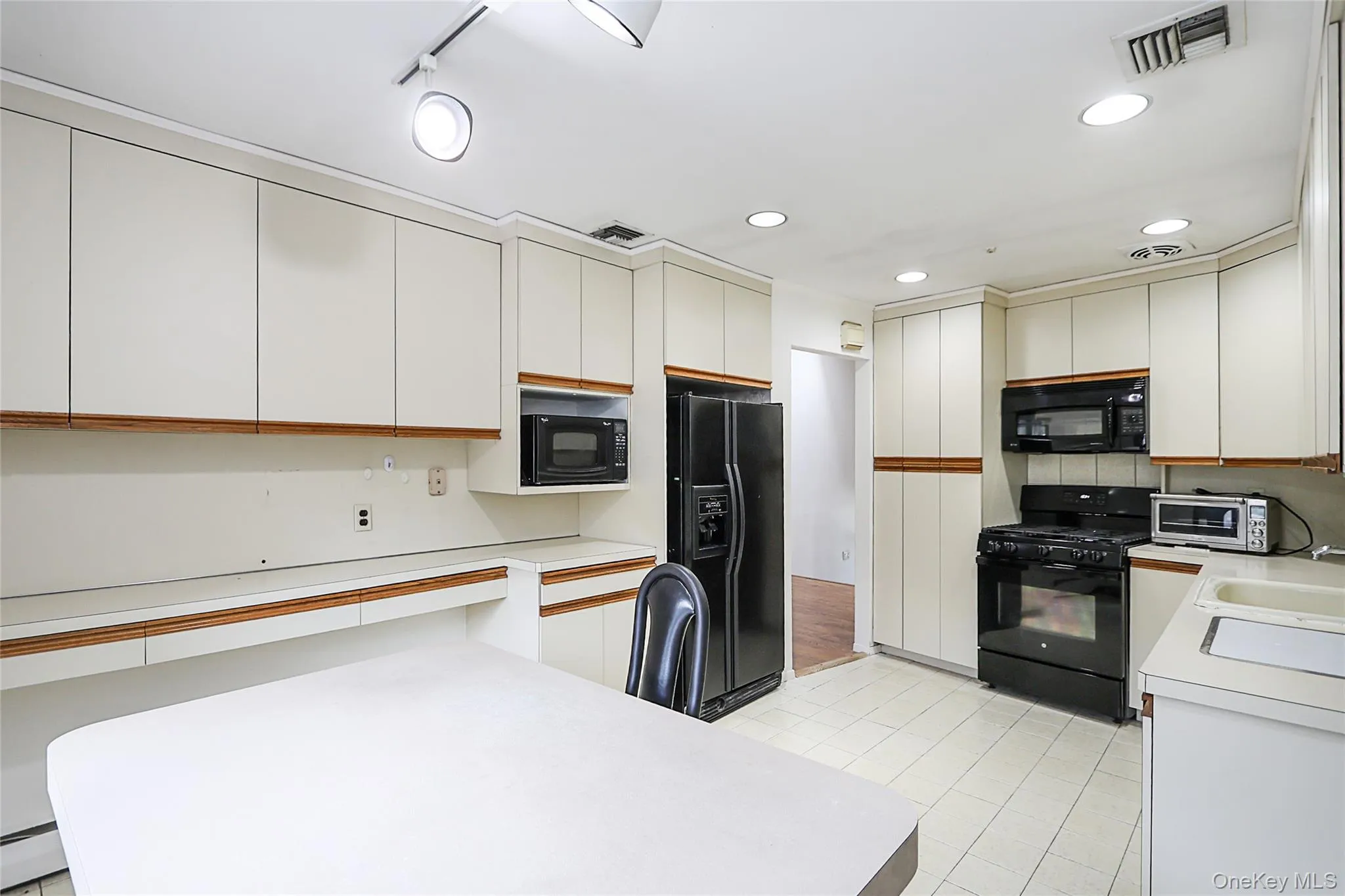 Kitchen with light countertops, black appliances, recessed lighting, light tile patterned floors, and white cabinetry Kitchen with light countertops, black appliances, recessed lighting, light tile patterned floors, and white cabinetry