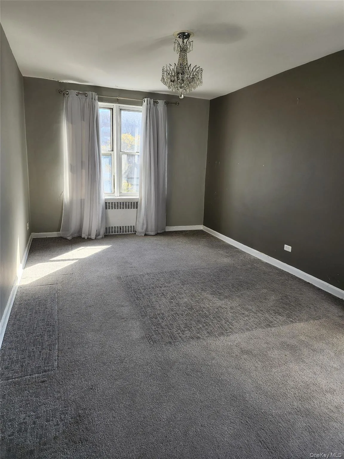 Carpeted empty room featuring radiator heating unit and a chandelier Carpeted empty room featuring radiator heating unit and a chandelier