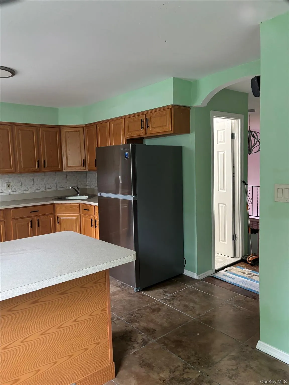 Kitchen featuring brown cabinetry, freestanding refrigerator, arched walkways, and tasteful backsplash Kitchen featuring brown cabinetry, freestanding refrigerator, arched walkways, and tasteful backsplash