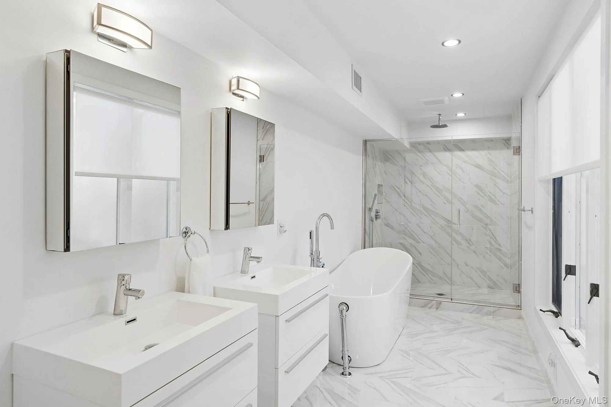 Bathroom featuring a stall shower, a freestanding bath, two vanities, recessed lighting, and light marble finish flooring Bathroom featuring a stall shower, a freestanding bath, two vanities, recessed lighting, and light marble finish flooring