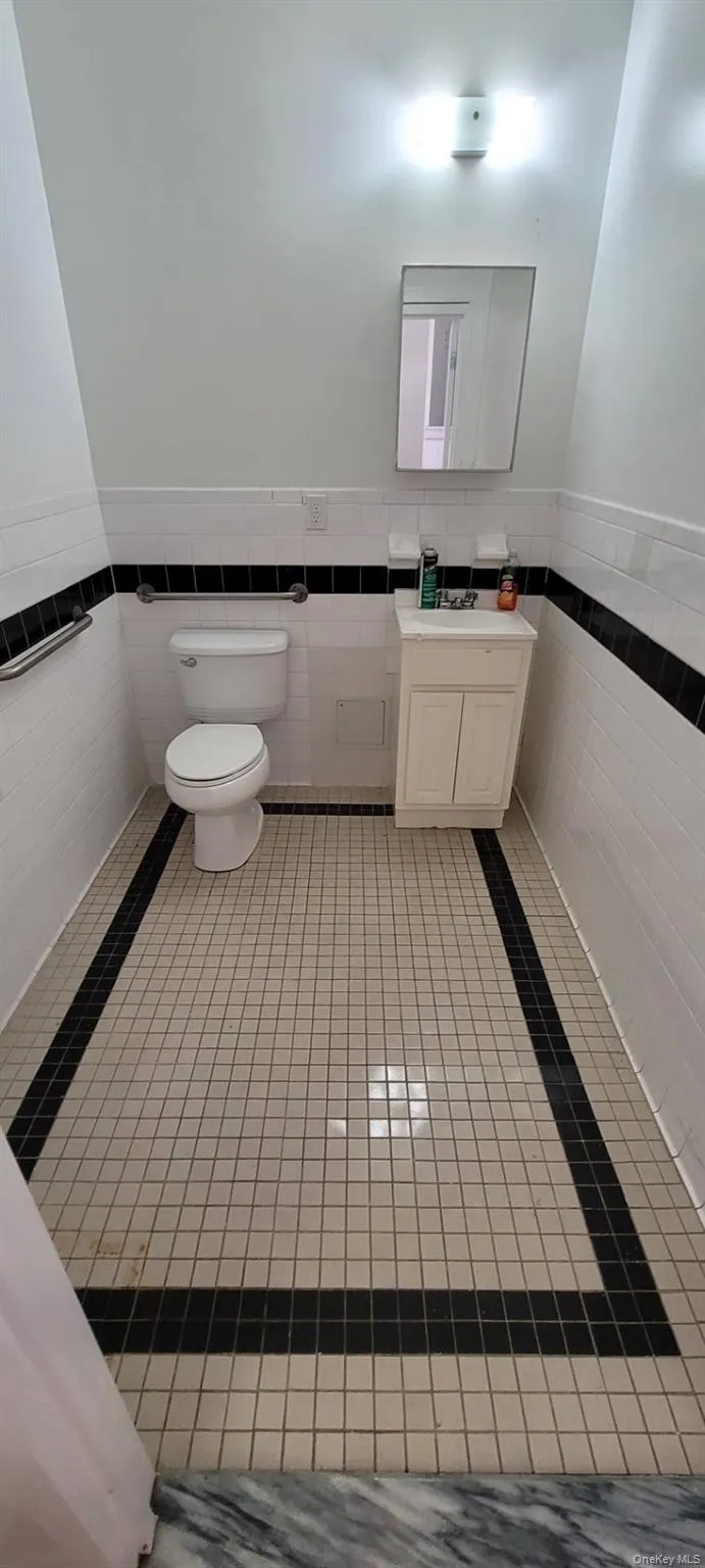 Half bath featuring tile walls, wainscoting, vanity, and light tile patterned floors Half bath featuring tile walls, wainscoting, vanity, and light tile patterned floors