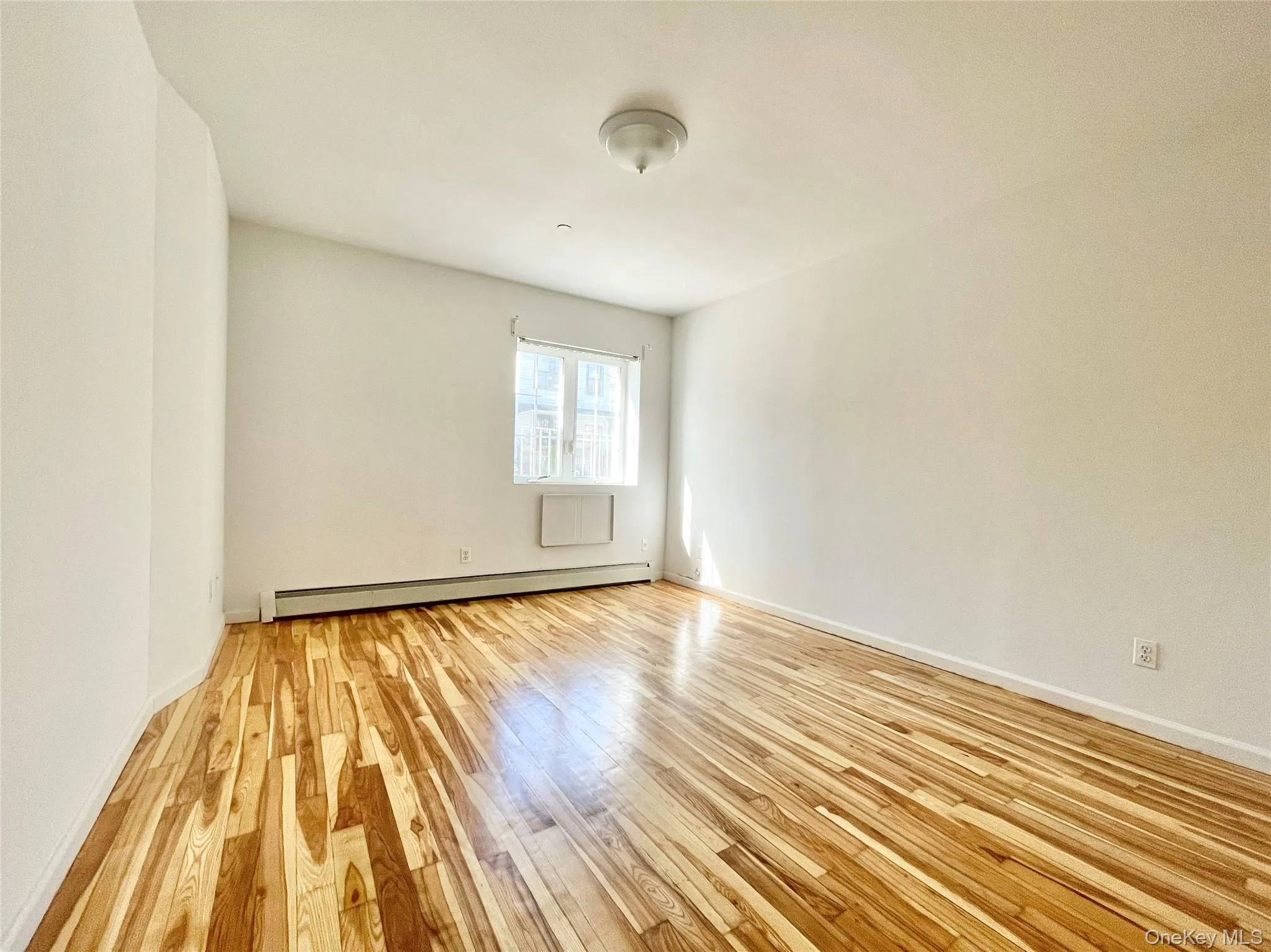 Empty room featuring light wood finished floors and a baseboard heating unit Empty room featuring light wood finished floors and a baseboard heating unit