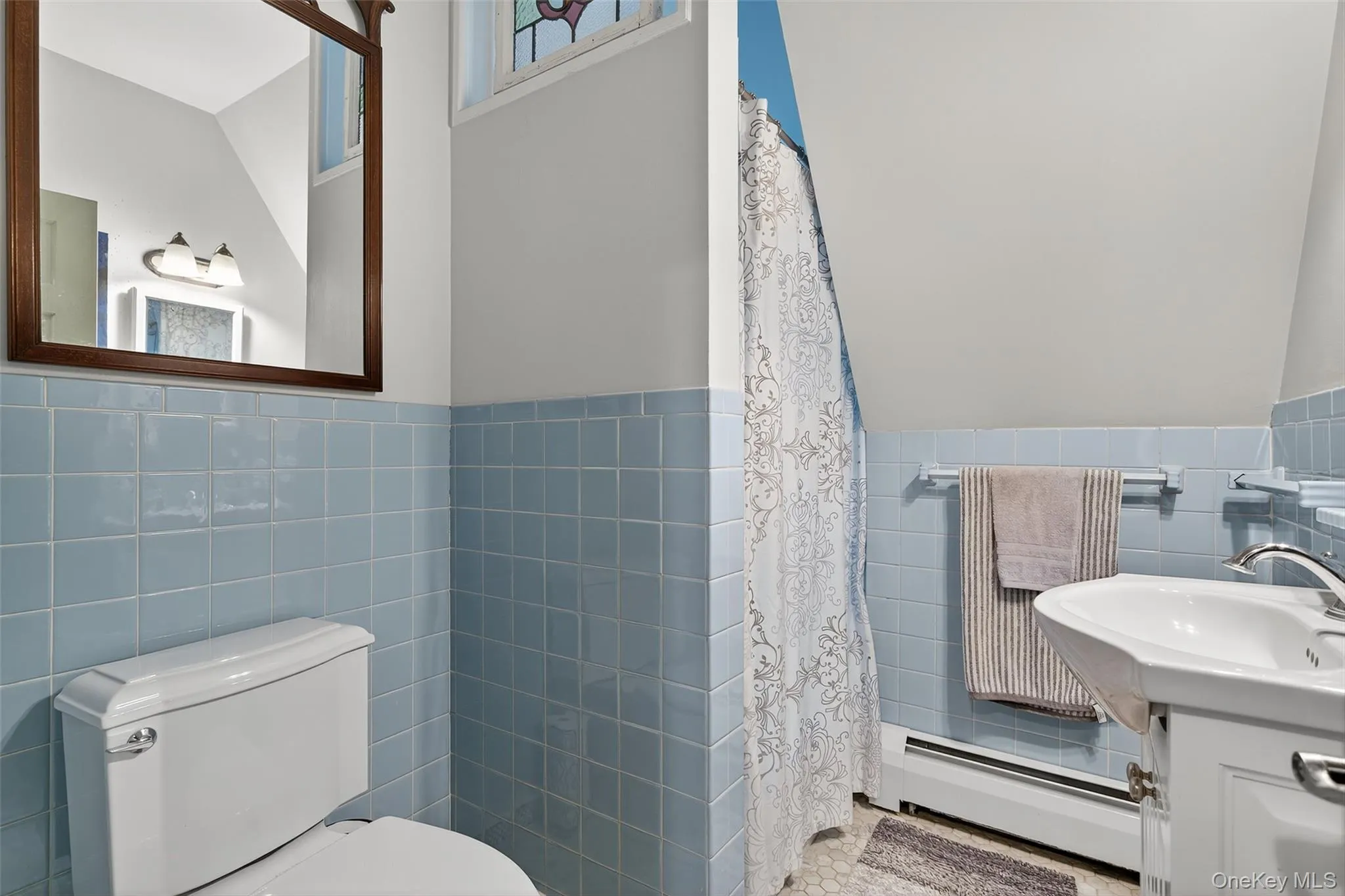 Bathroom with tile walls, a baseboard radiator, wainscoting, vanity, and curtained shower Bathroom with tile walls, a baseboard radiator, wainscoting, vanity, and curtained shower