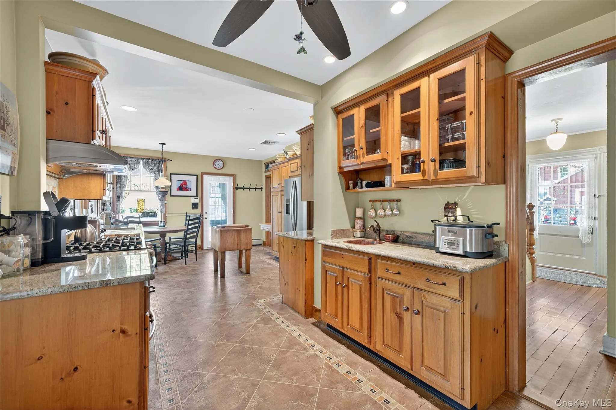 Kitchen featuring decorative light fixtures, glass insert cabinets, inlaid floor details, brown cabinetry, and light tile patterned floors Kitchen featuring decorative light fixtures, glass insert cabinets, inlaid floor details, brown cabinetry, and light tile patterned floors