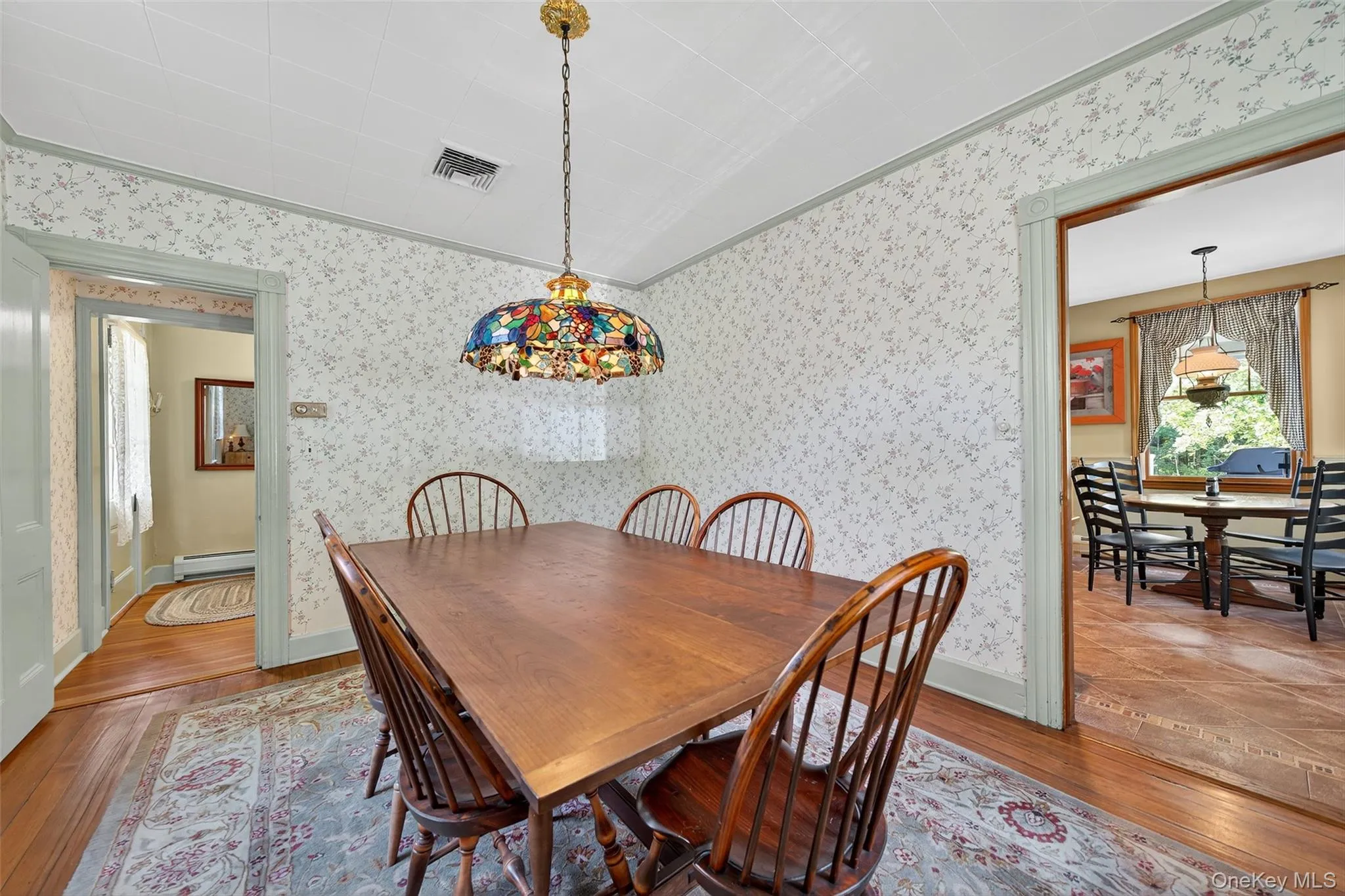 Dining space with hardwood / wood-style floors, ornamental molding, a baseboard heating unit, and wallpapered walls Dining space with hardwood / wood-style floors, ornamental molding, a baseboard heating unit, and wallpapered walls